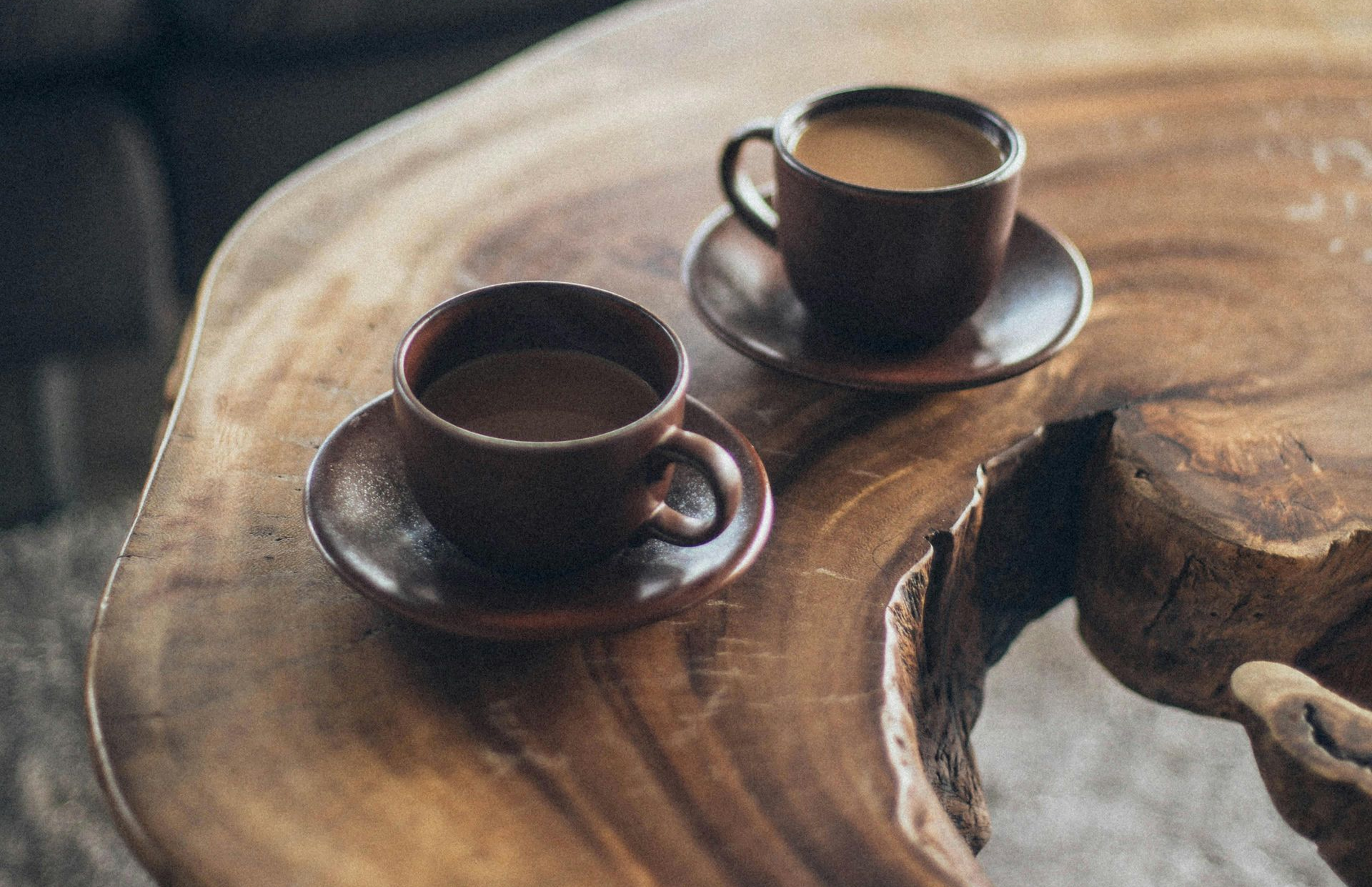 Twee bruine koffiekopjes op schoteltjes staan op een rustieke houten tafel.