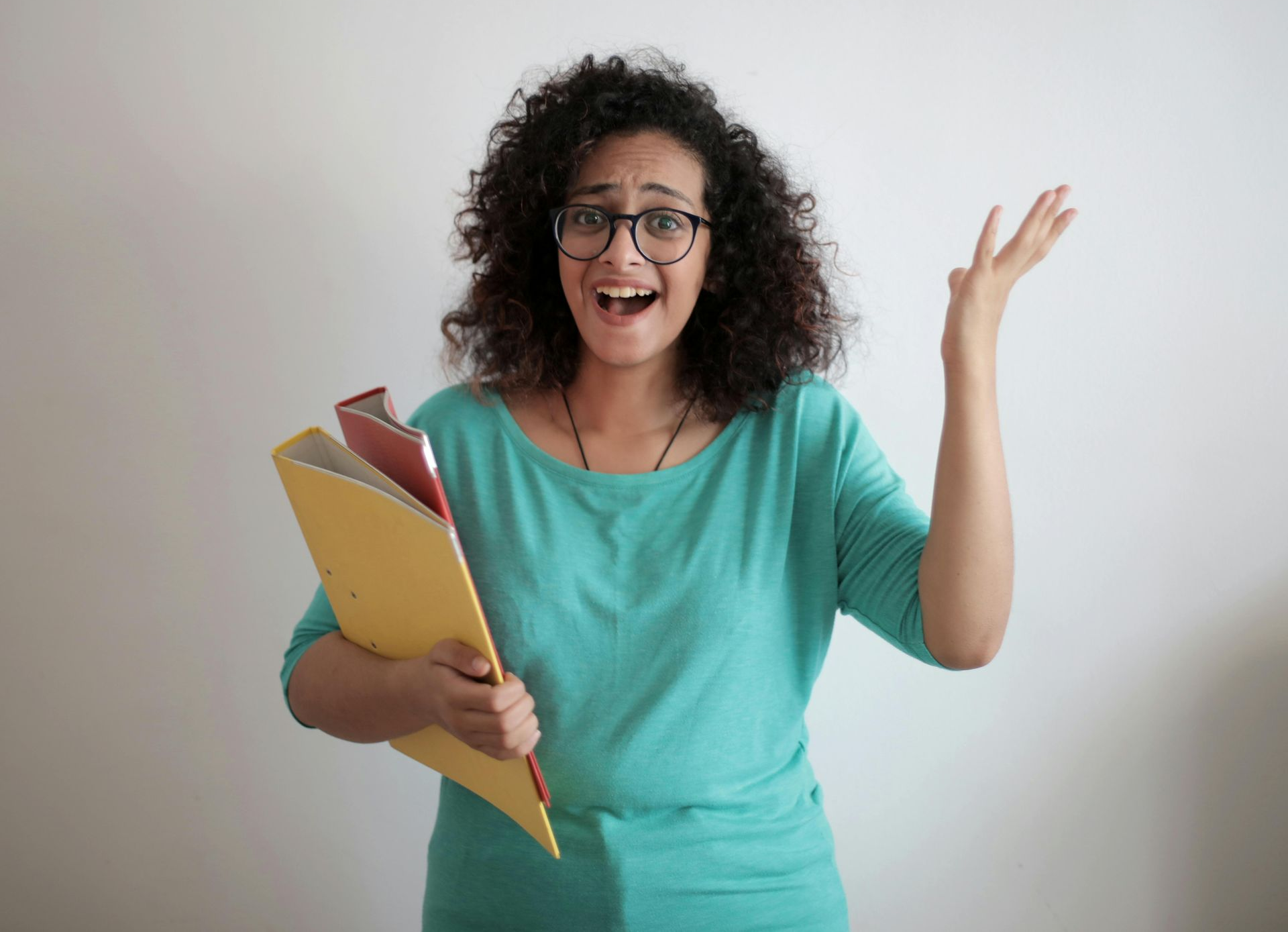 Vrouw in een turquoise top met bril, verbaasde uitdrukking, houdt dossiers vast, arm omhoog.