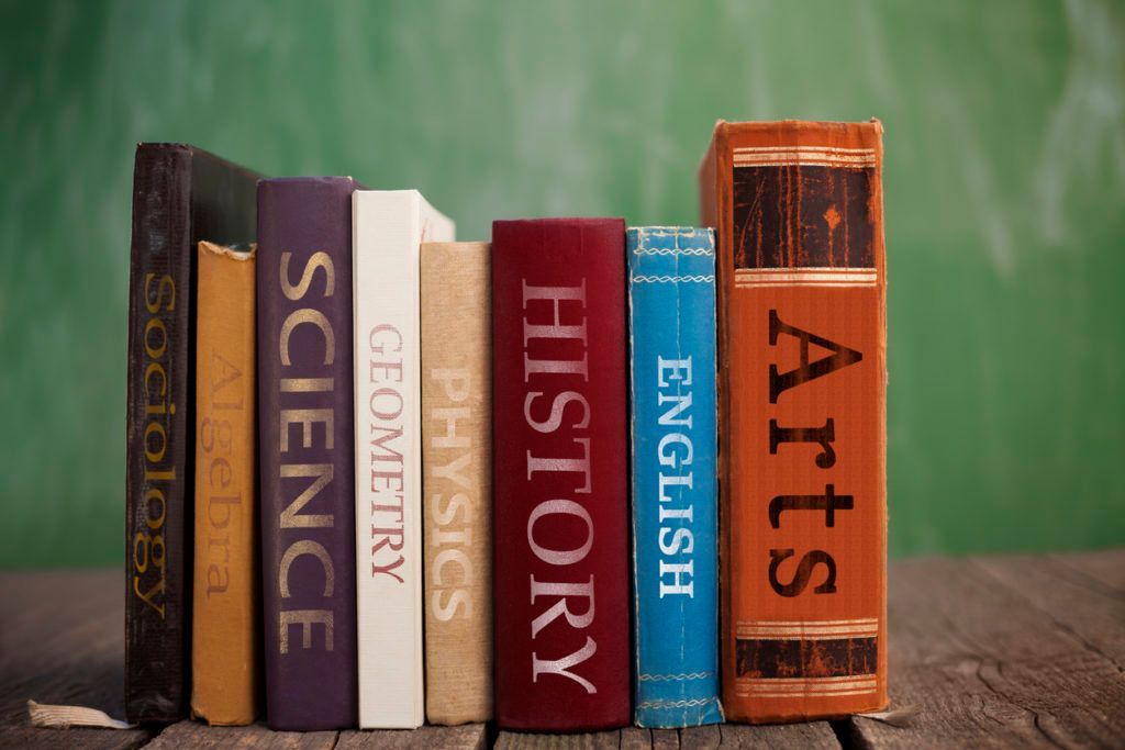 Books labeled with subjects stand on a wooden surface against a green background.
