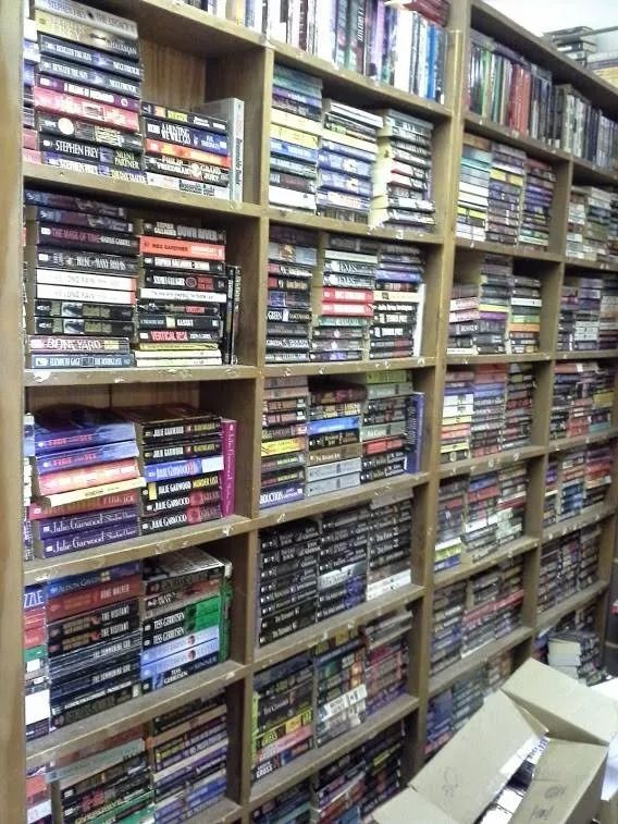 Bookshelves filled with stacked books; warm, wooden shelves in a shop or library.