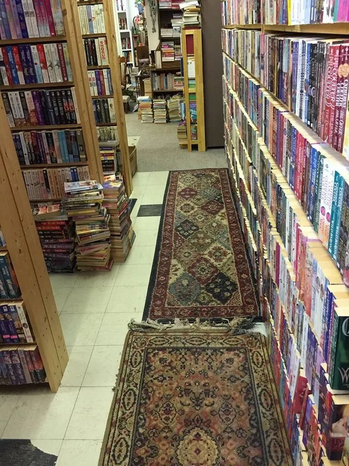 Narrow bookstore aisle lined with bookshelves, books, and area rugs on the floor.