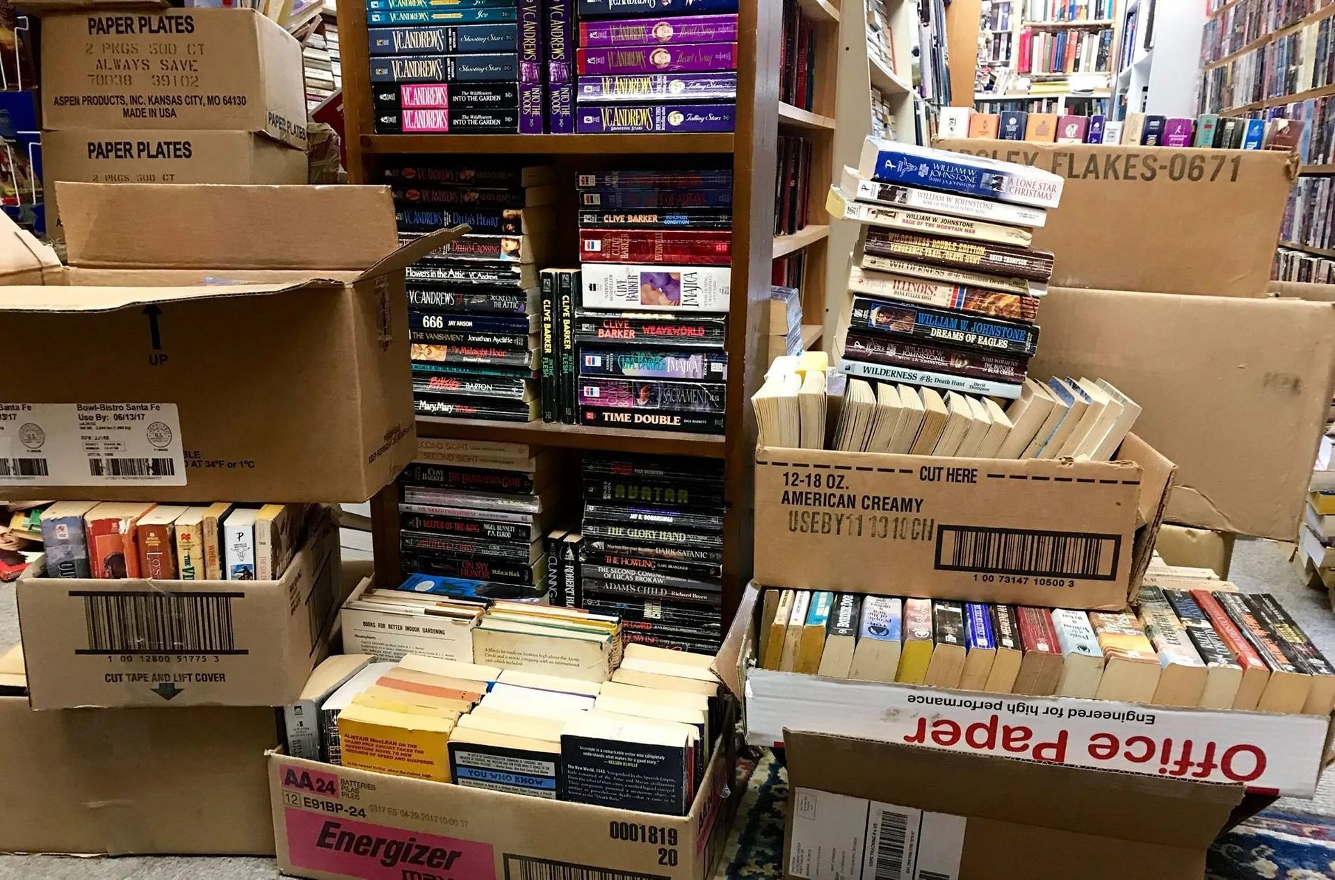 Bookshelves and boxes overflowing with books in a bookstore, with various colors and titles visible.