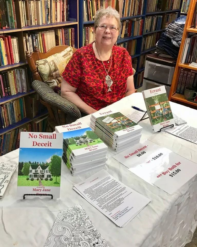 Woman at a table with books, signing them in a bookstore. Books are stacked with cover art.
