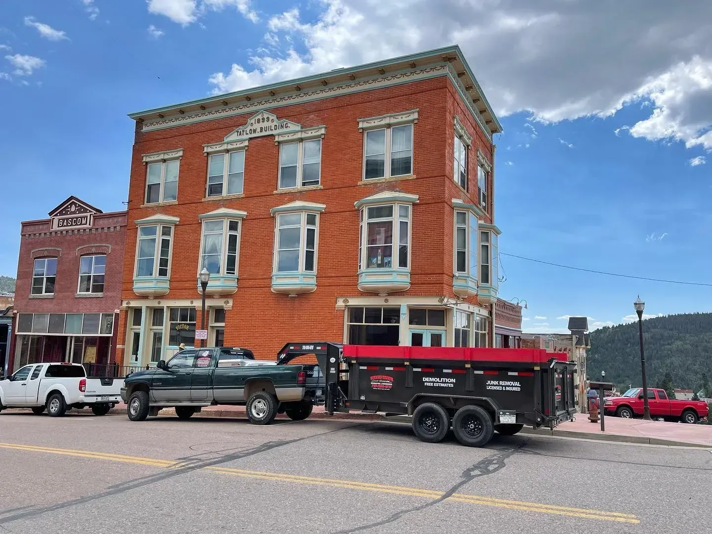 A truck is pulling a dumpster in front of a large brick building.
