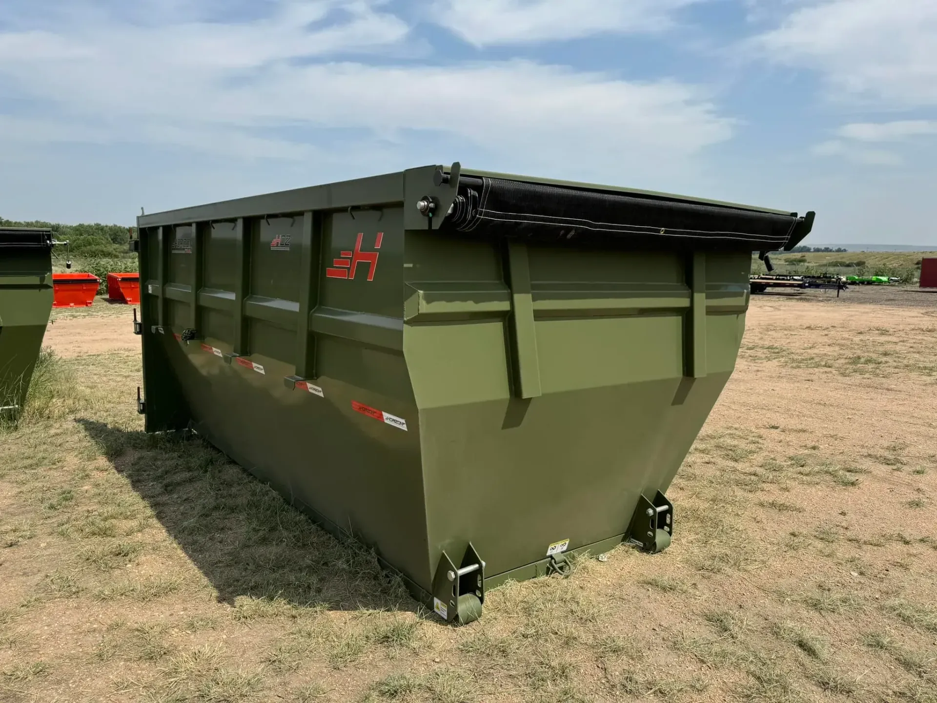 A green dumpster is sitting in the middle of a field.