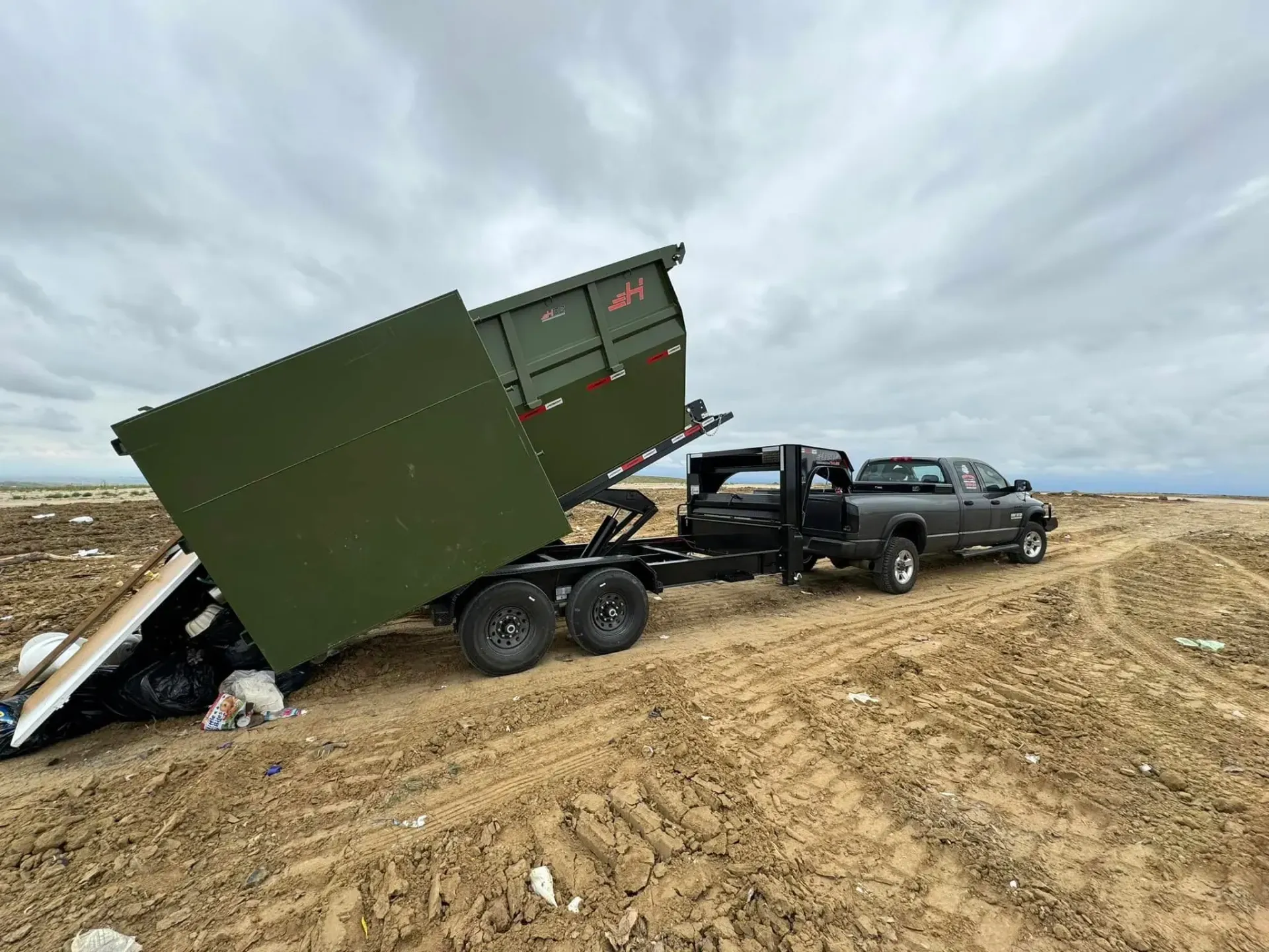 A dumpster is being towed by a truck in a dirt field.