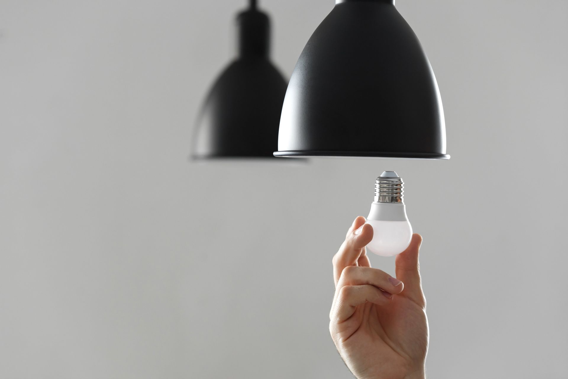 Hand replacing lightbulb under a black pendant lamp. White background.