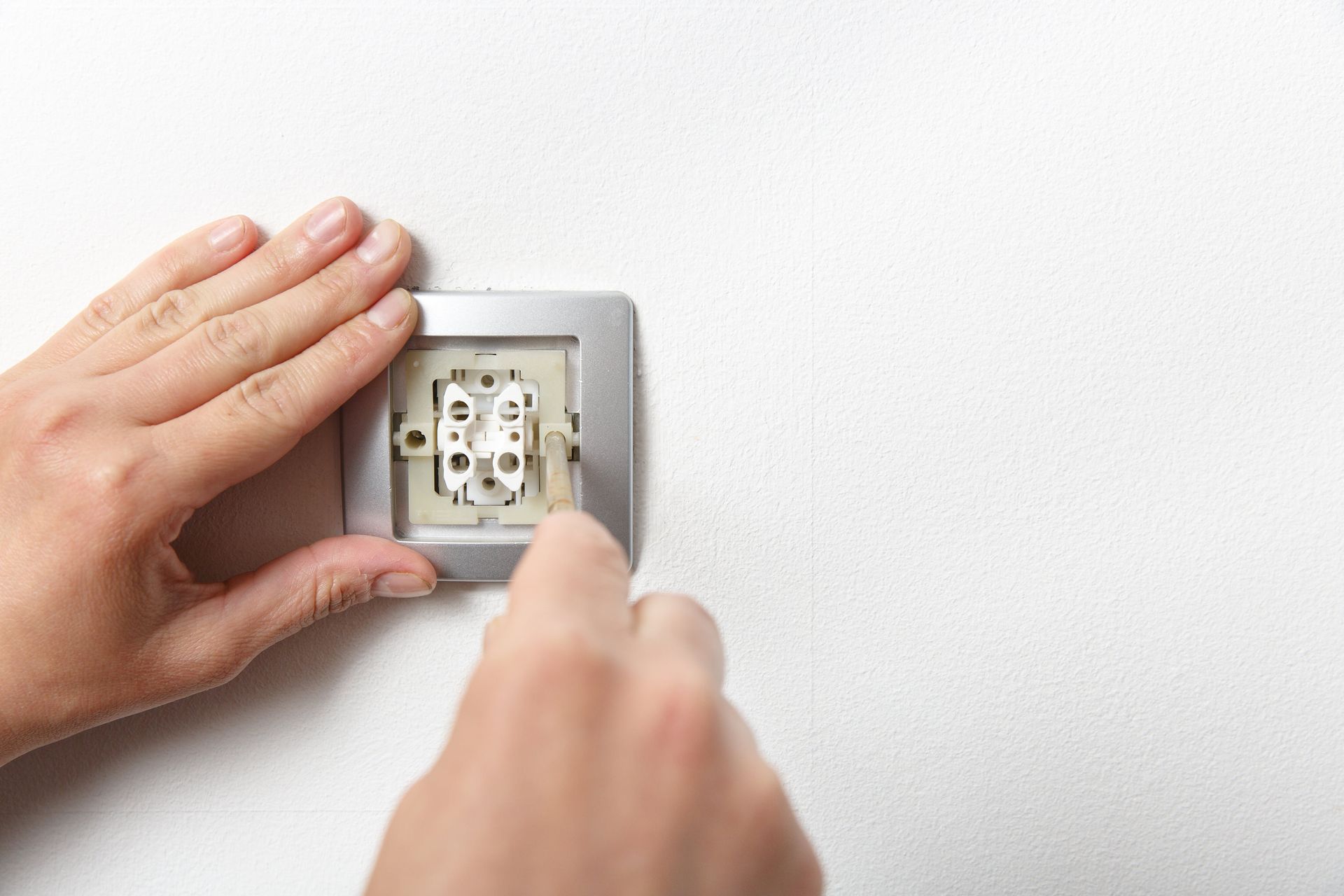 Hands installing a light switch on a white wall.