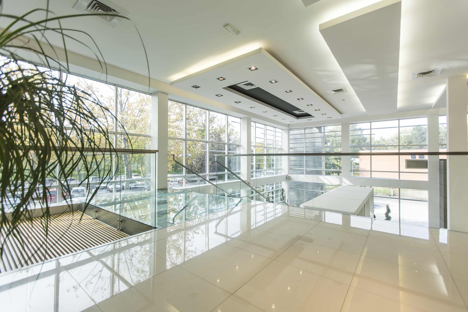 Bright, modern office lobby with large windows, white tile floor, and glass railings.