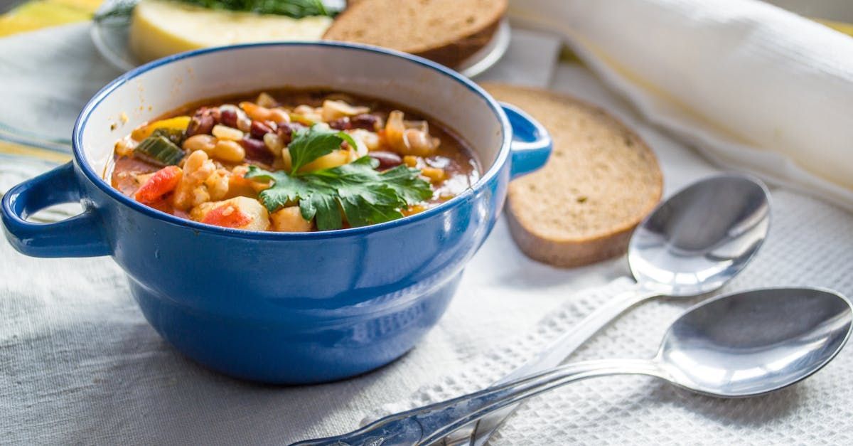 A bowl of soup is sitting on a table next to spoons and bread.