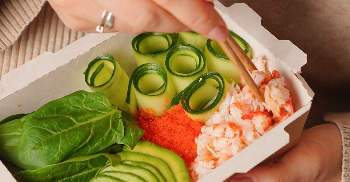 A person is holding a box of food with chopsticks.