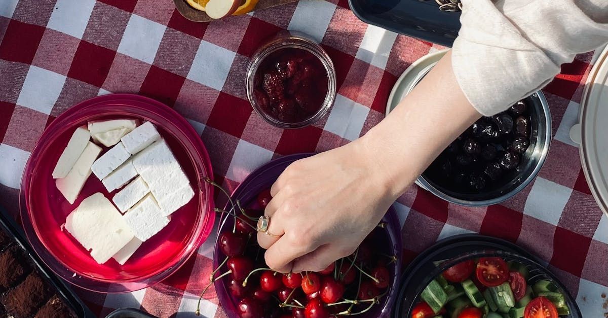 A person is picking cherries from a bowl on a picnic table.