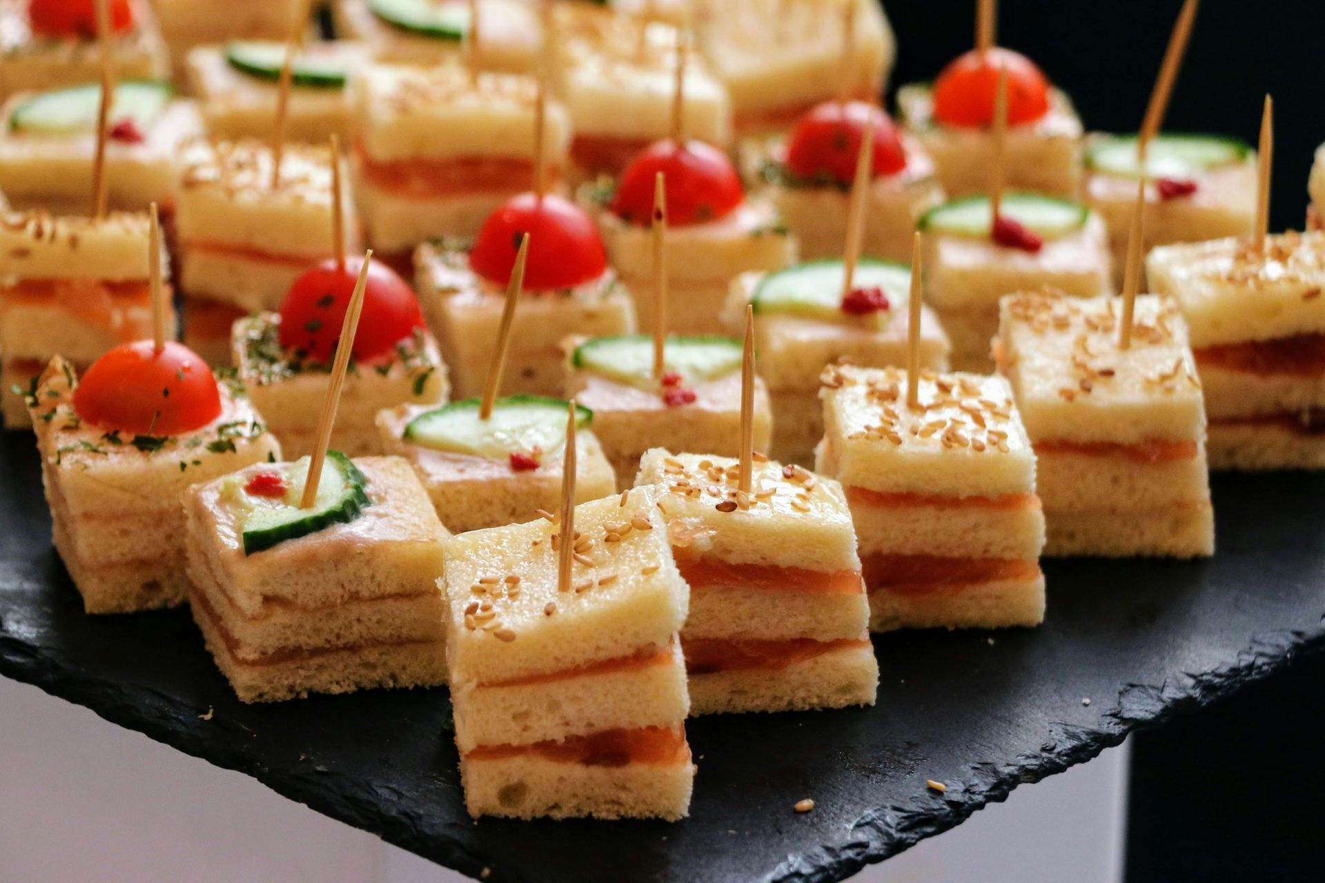 A tray of small sandwiches with tomatoes and cucumbers on toothpicks.