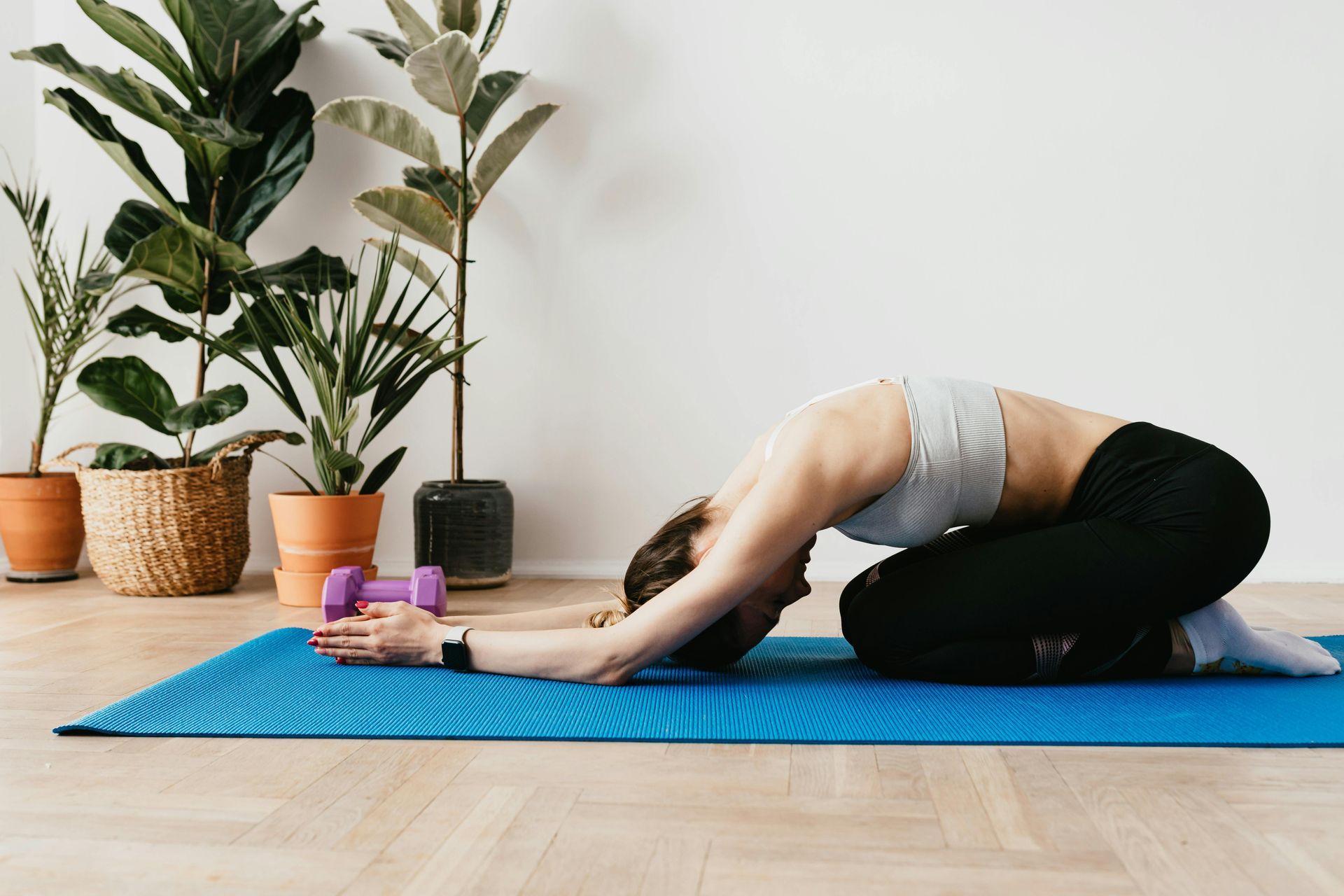 A woman is kneeling on a yoga mat with a dumbbell.