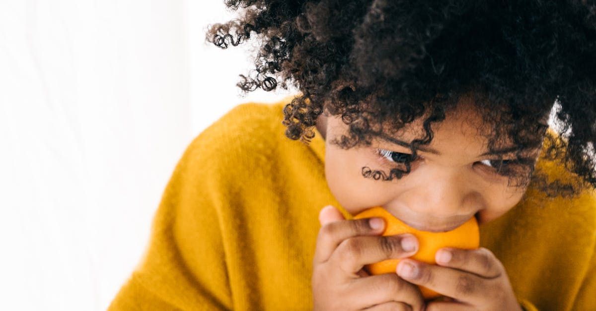 A young girl in a yellow sweater is eating an orange.