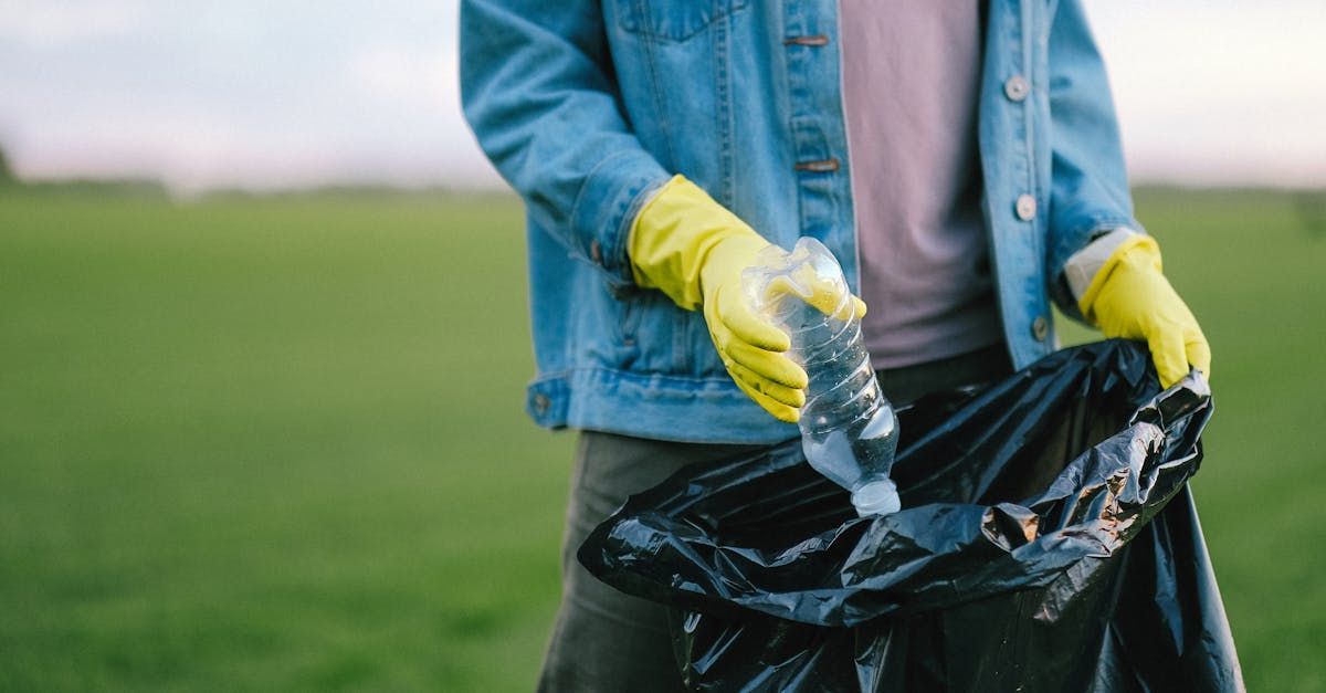 A person wearing yellow gloves is holding a plastic bottle and a black bag.