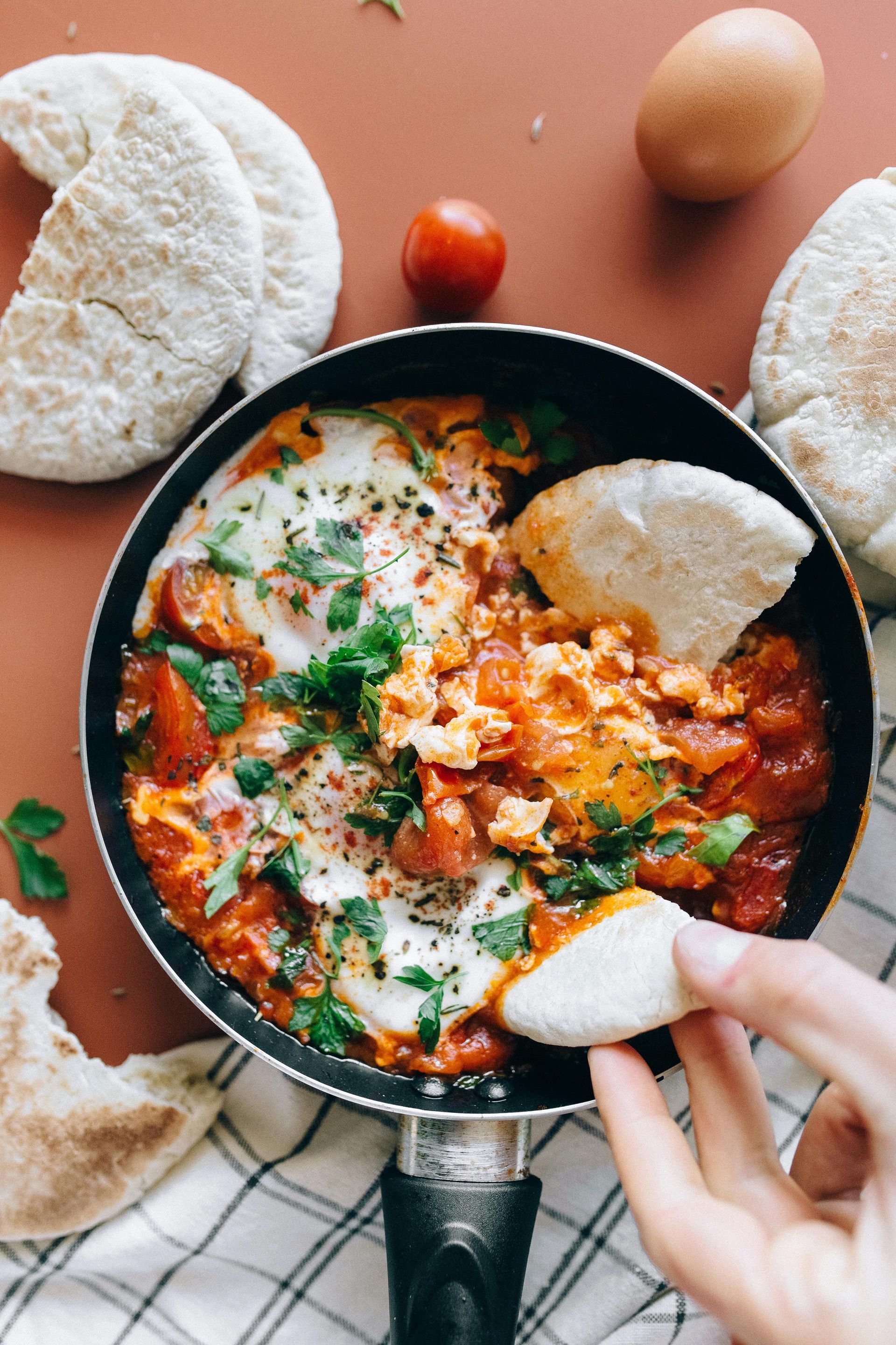 A person is dipping a piece of bread into a pan of food.