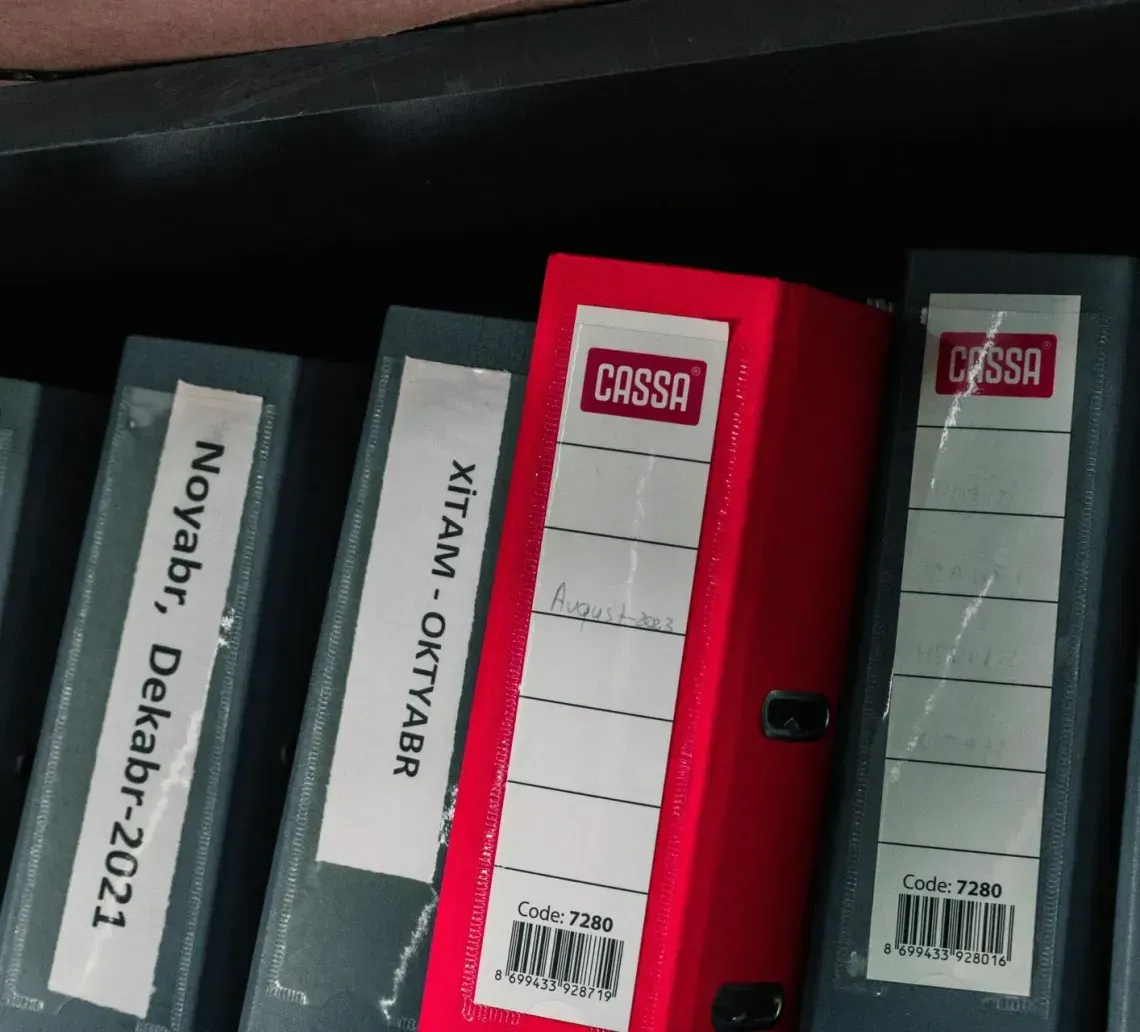 A shelf with gray and red binders labeled with text and dates, including 