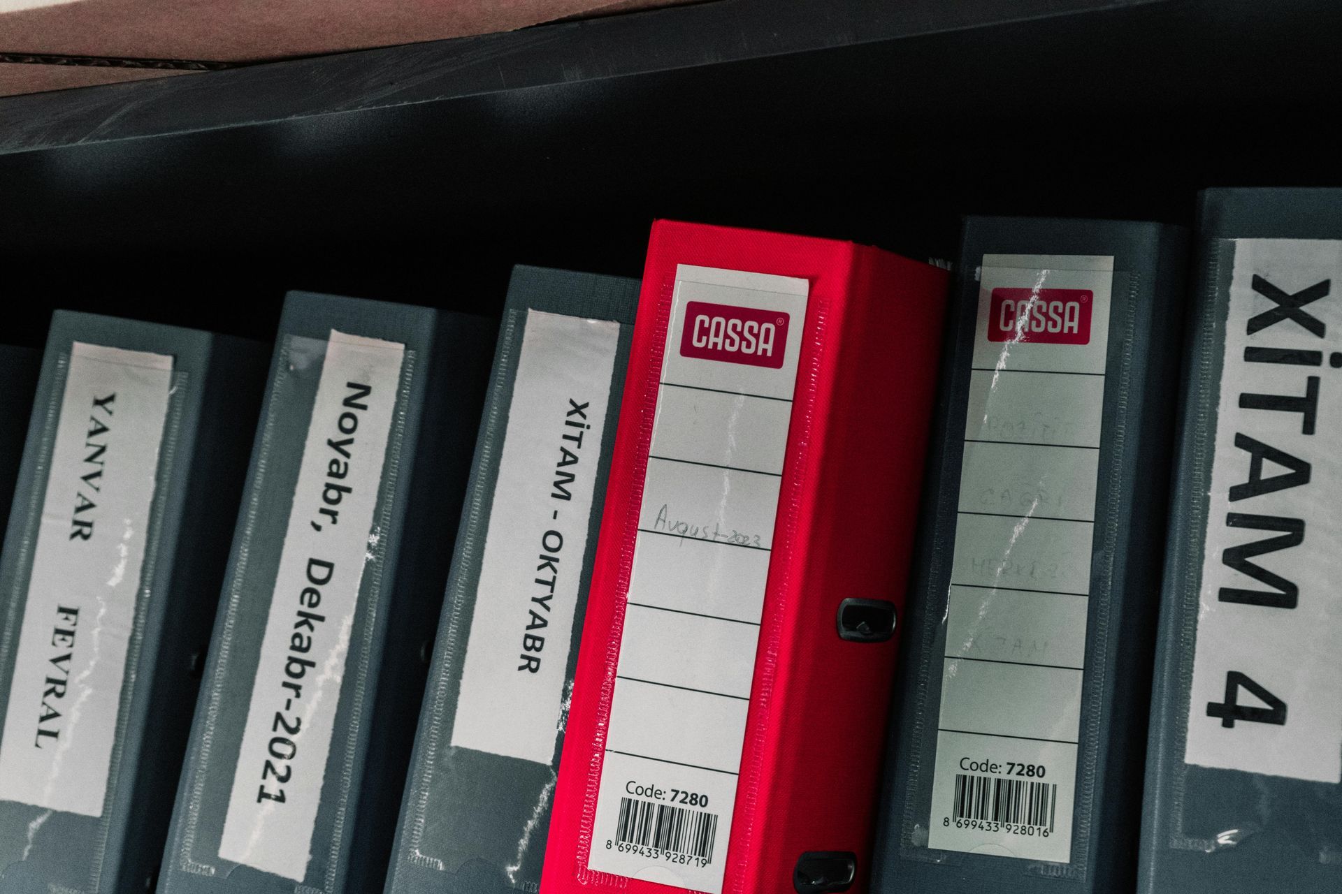 A shelf with gray and red binders labeled with text and dates, including