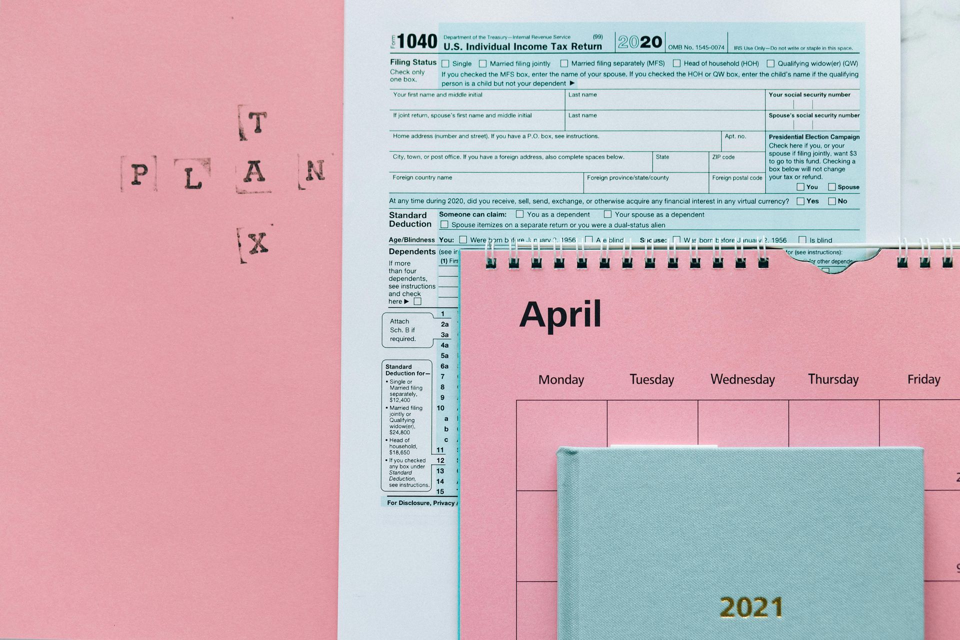 A US 1040 tax form, a pink calendar for April 2021, and a blue notebook, with the words 
