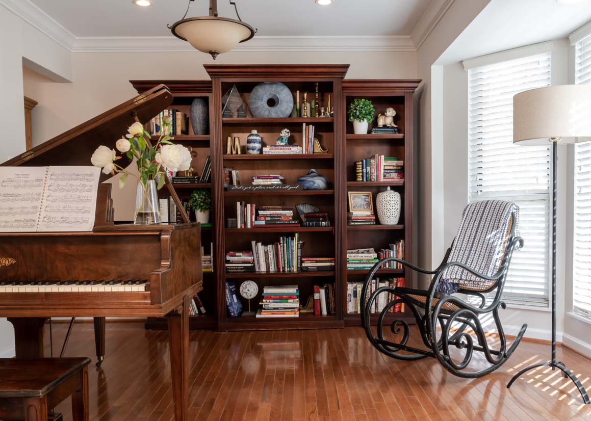 A living room with a piano , rocking chair , and bookshelf.