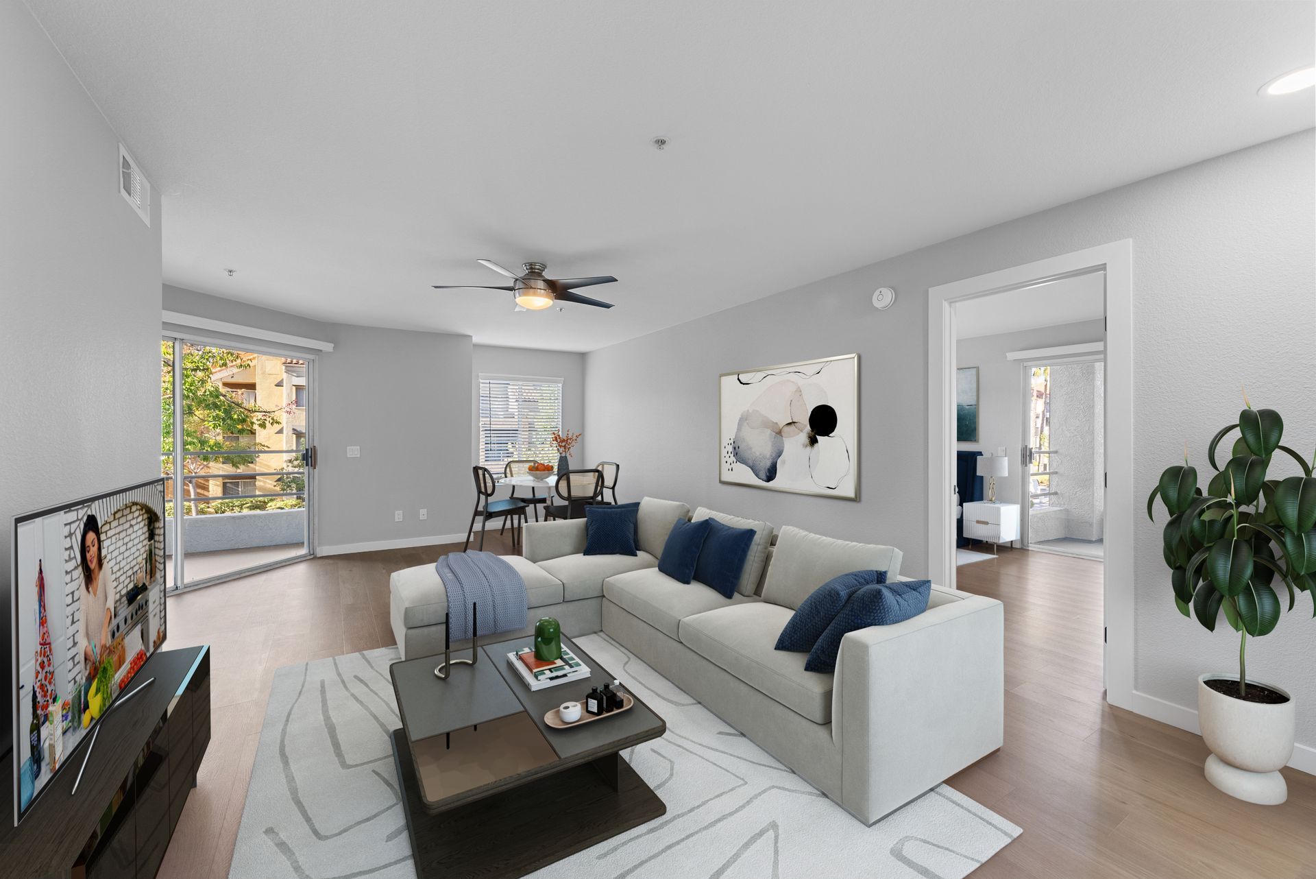 Living room with gray walls, sectional sofa, rug, dining area, balcony access, and potted plant.