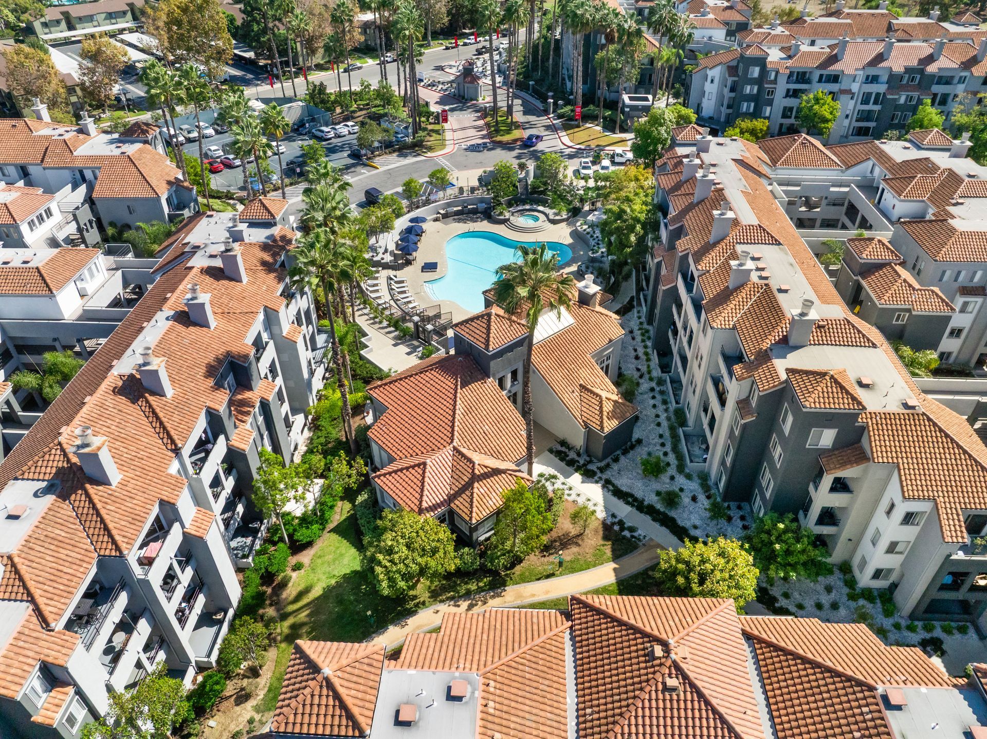 Aerial view of apartment complex with a pool, brown tiled roofs, and lush landscaping.
