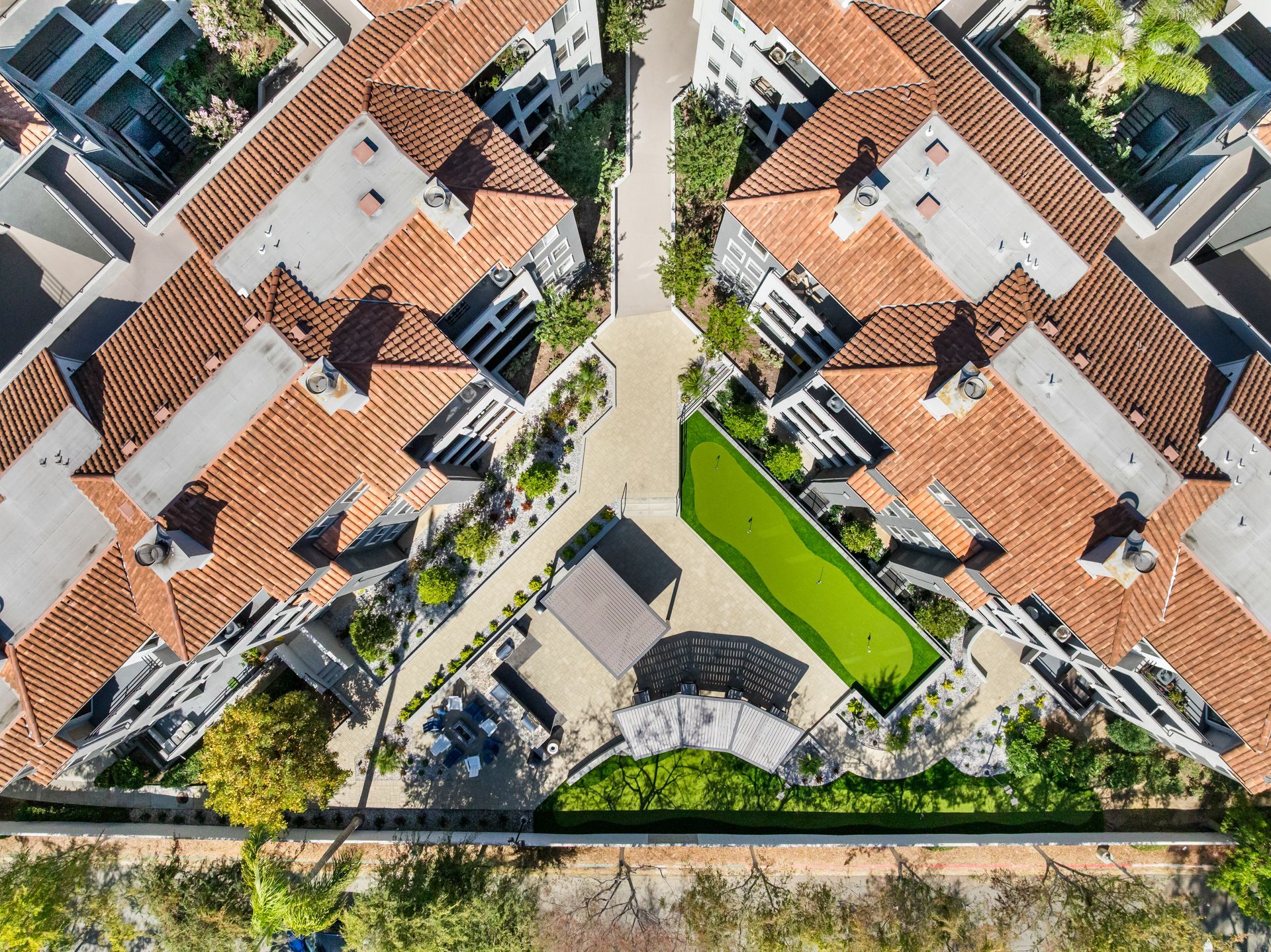 Aerial view of apartment complex with terracotta tile roofs, green courtyard, and pathway.