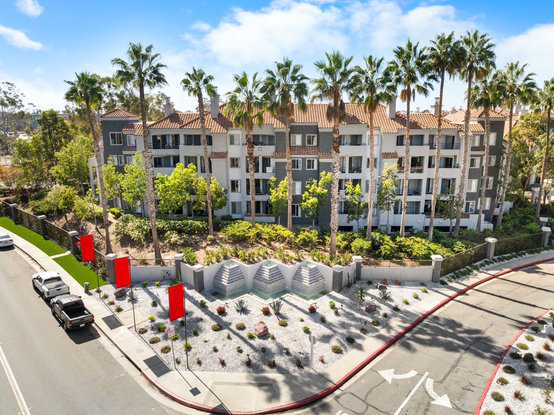 Multi-story apartment building with palm trees in front; red accent panels.