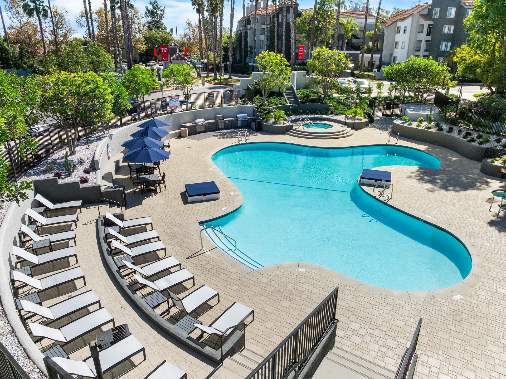 Pool with lounge chairs, umbrellas, and a jacuzzi in a landscaped courtyard.