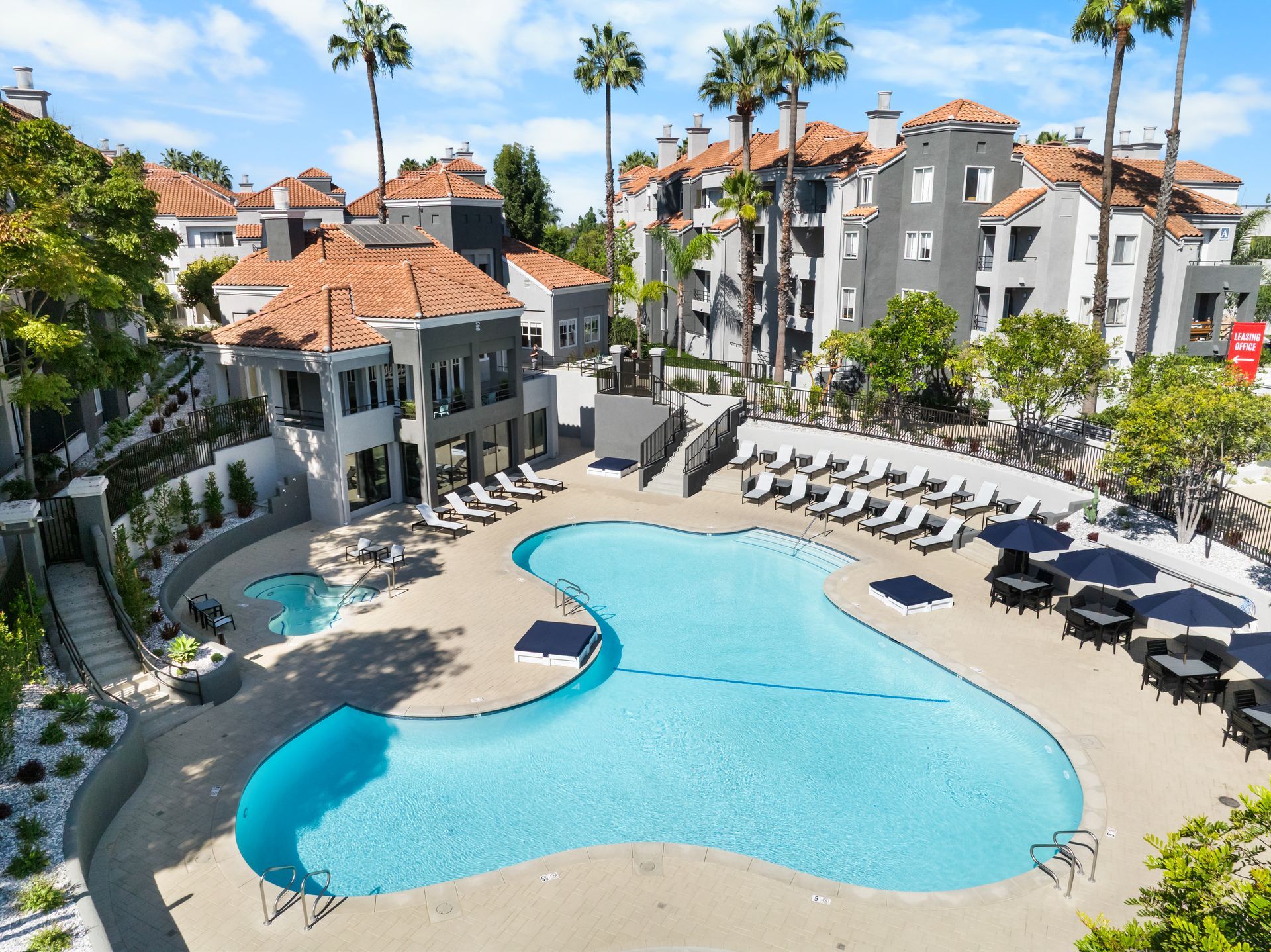 Swimming pool with lounge chairs surrounded by apartments and palm trees.