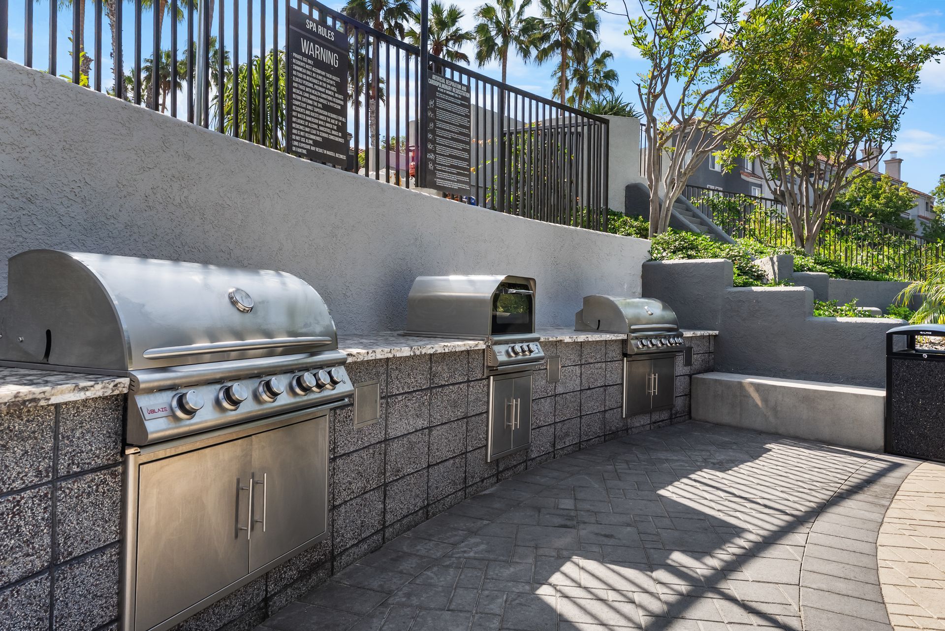 Outdoor grilling area with stainless steel grills, stone block counter, and tiered concrete steps.