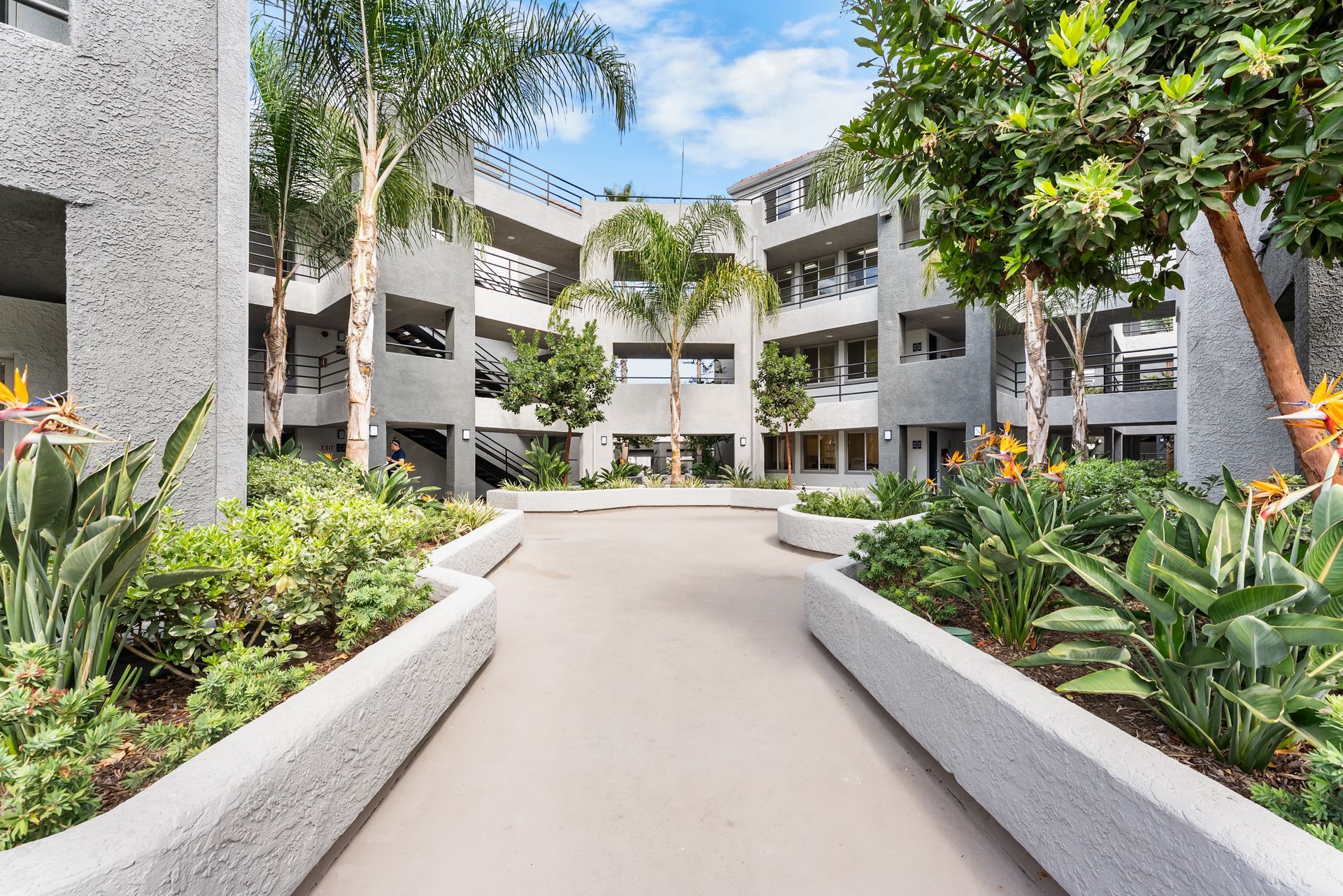 Courtyard with buildings, trees, and gardens; a walkway leads toward the center of the complex.