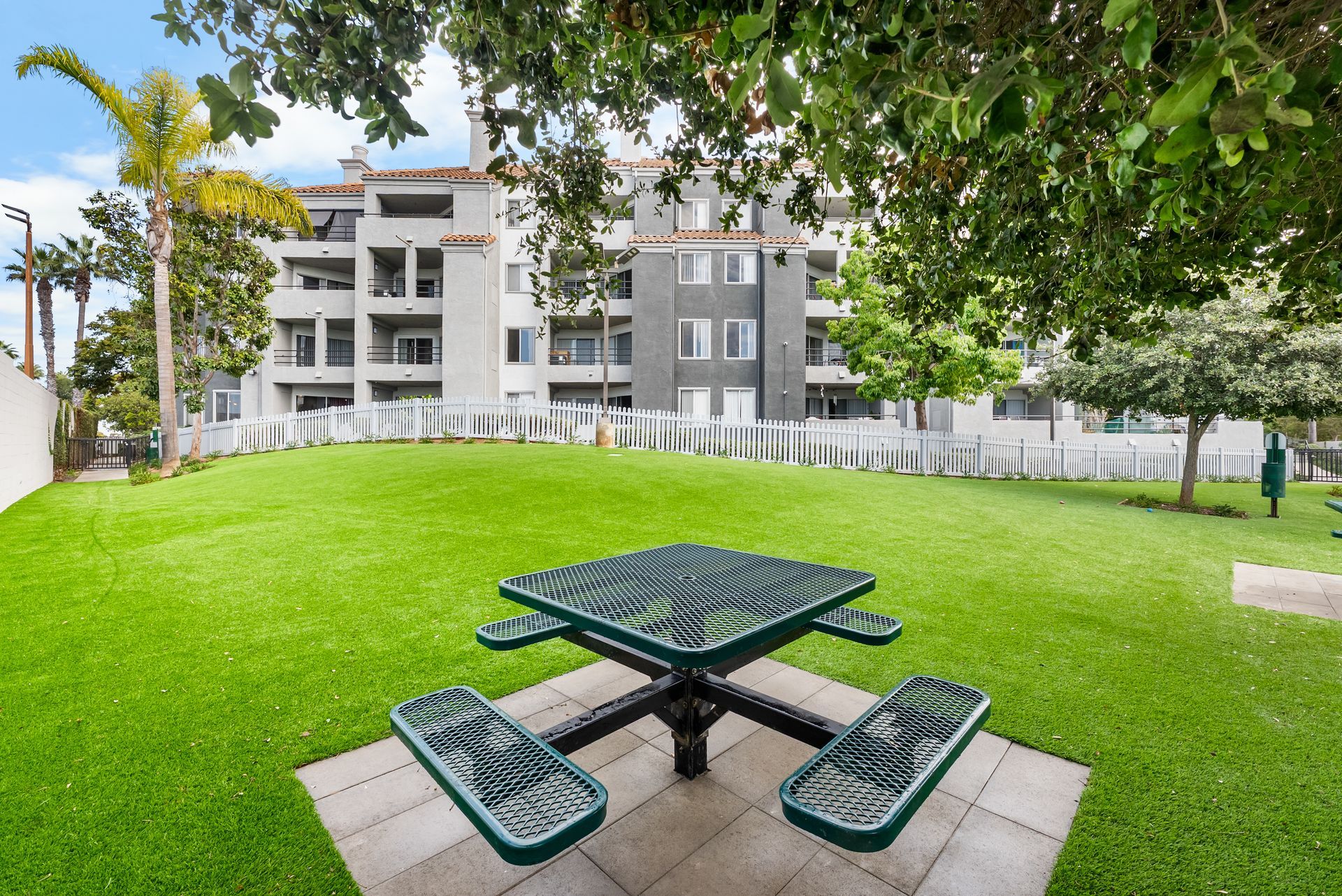 Picnic table on green dog park lawn in front of an apartment building.