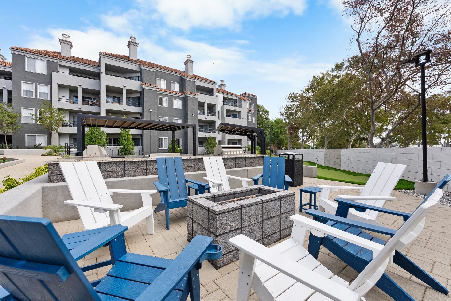Outdoor seating area with fire pit, blue and white chairs, and apartment building in the background.