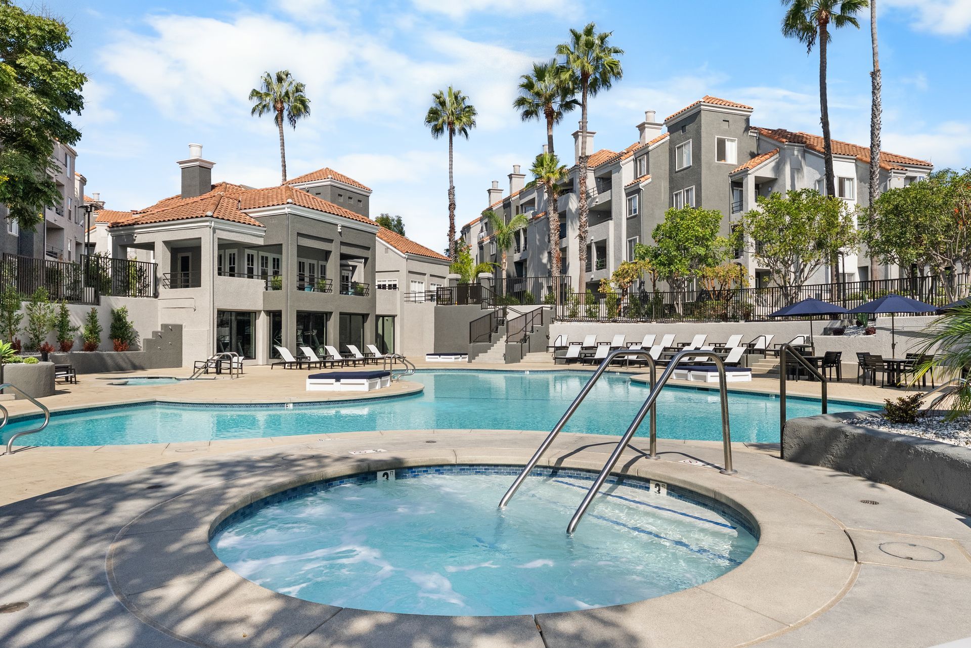 Swimming pool and jacuzzi at apartment complex with palm trees. Sunny day.
