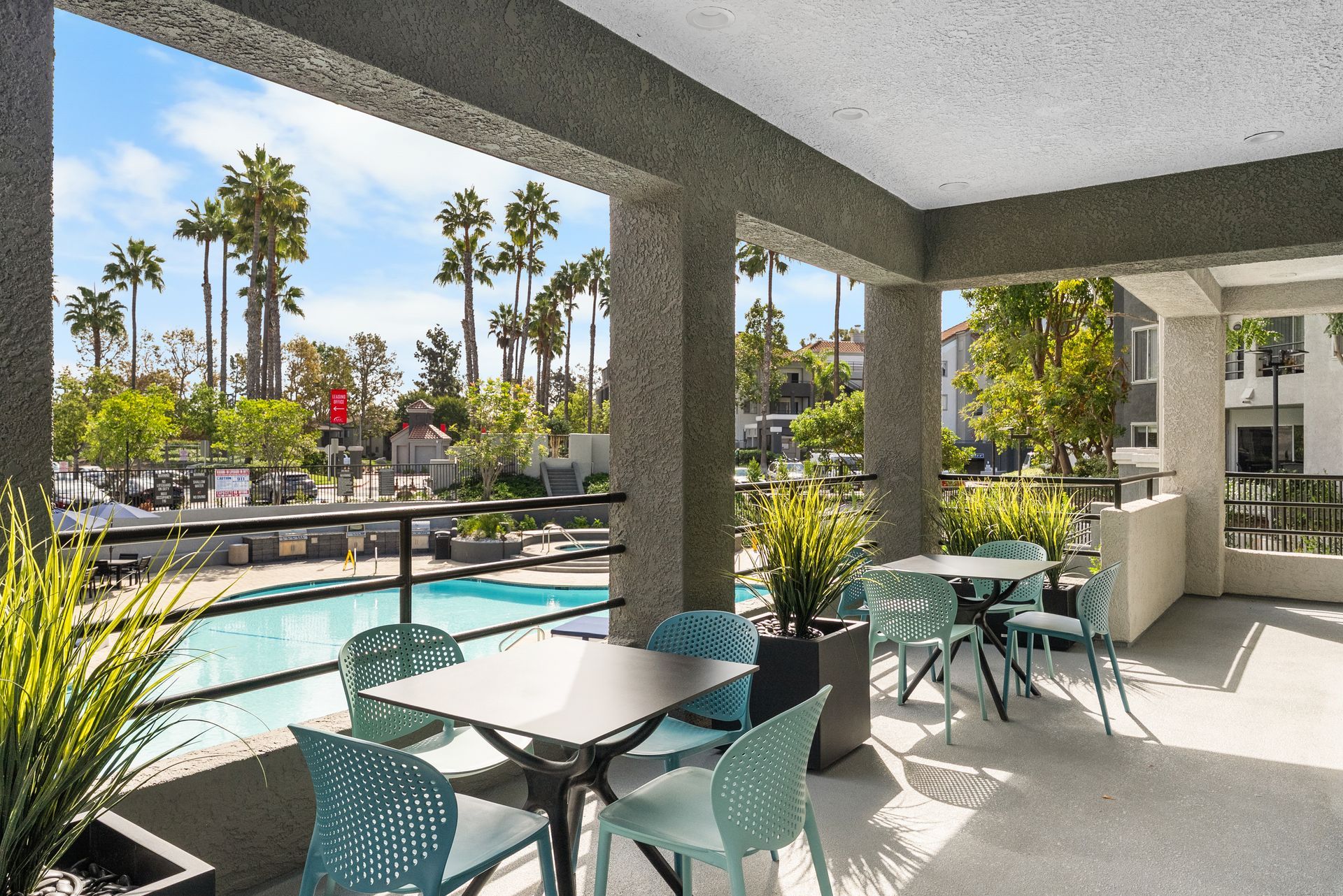 Patio with teal chairs and tables overlooking a pool and palm trees.