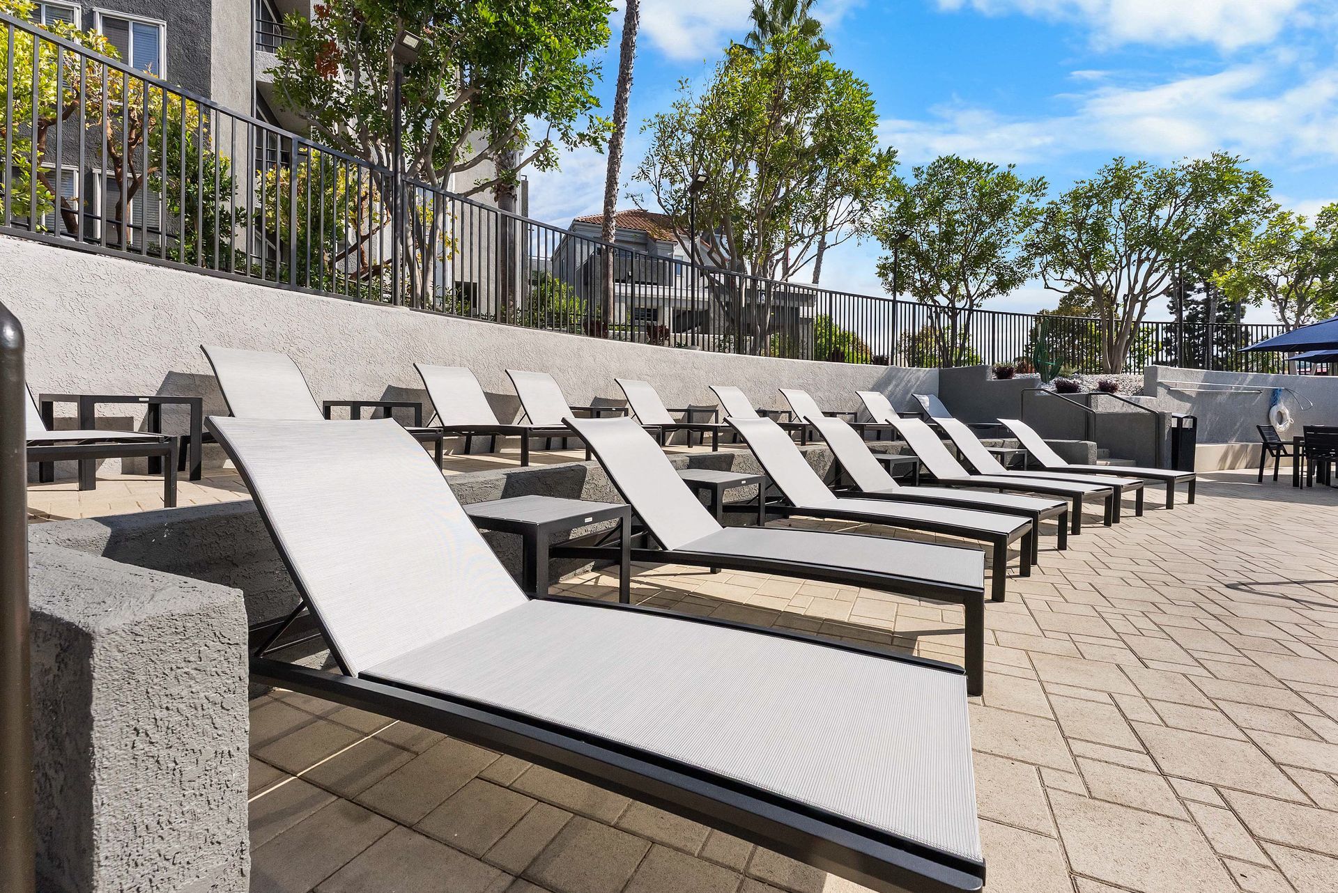 Row of gray lounge chairs on a terraced patio, overlooking a pool area.