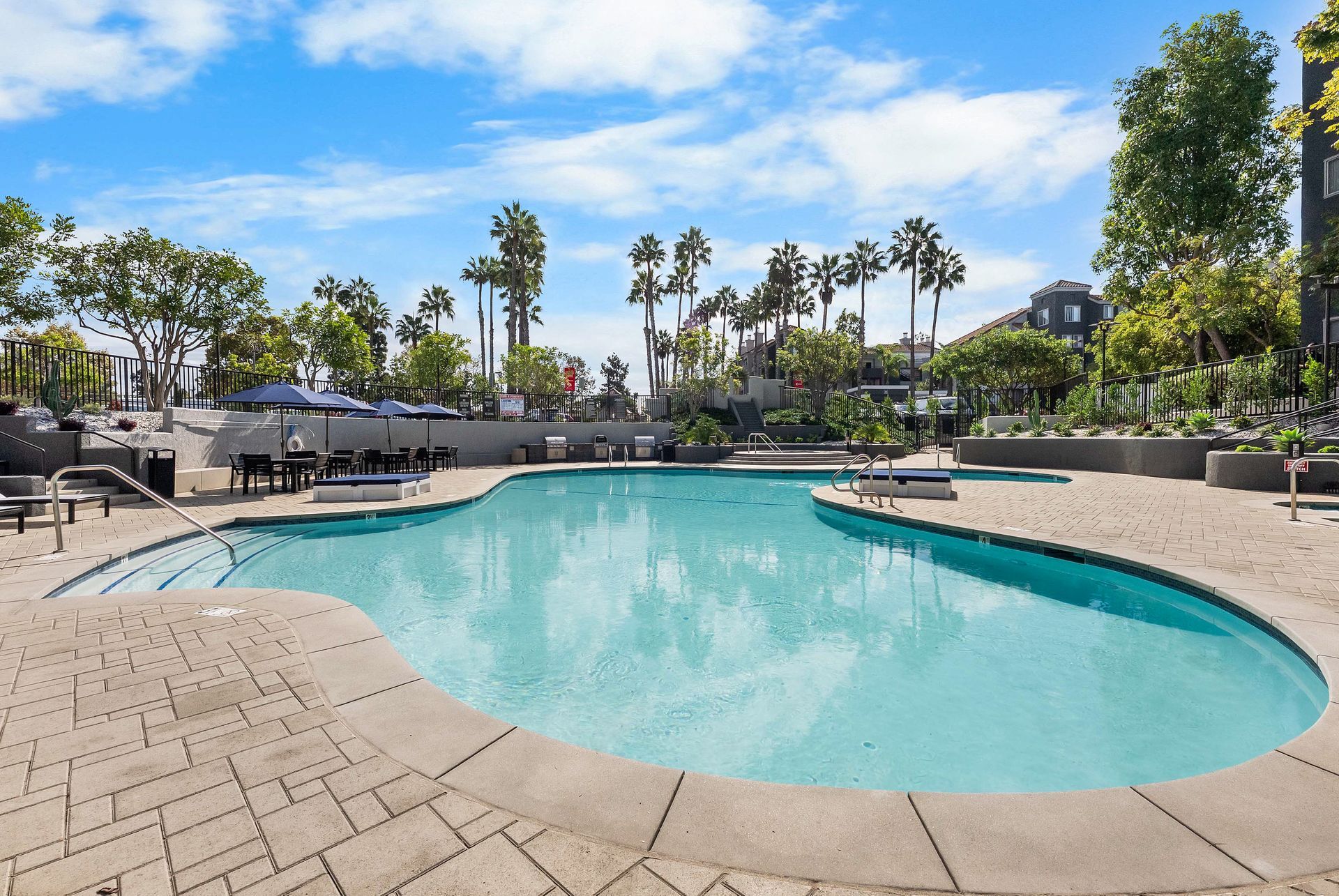 Pool area with turquoise water, lounge chairs, and palm trees under a bright blue sky.