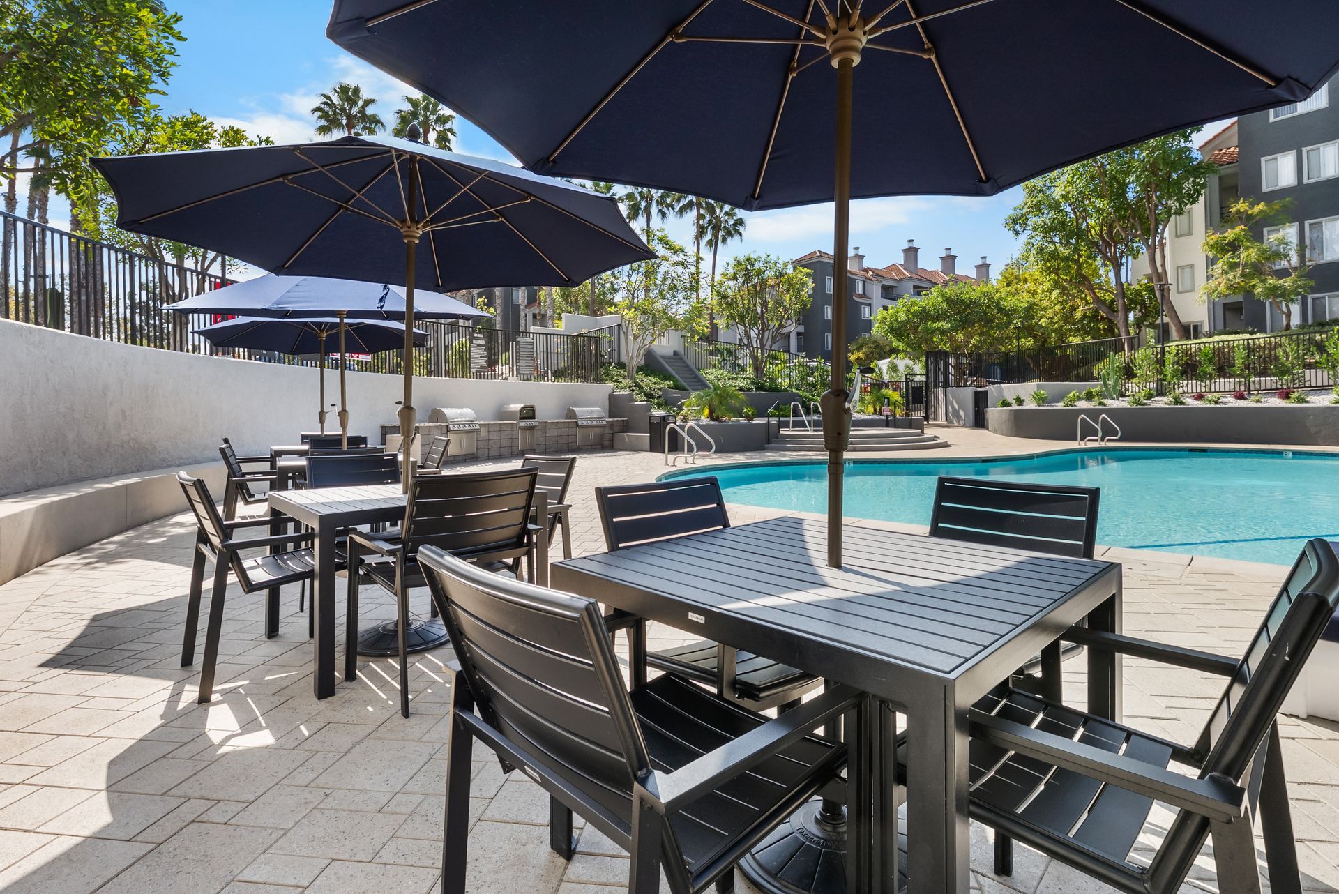 Outdoor seating area with tables, chairs, and umbrellas by a swimming pool.