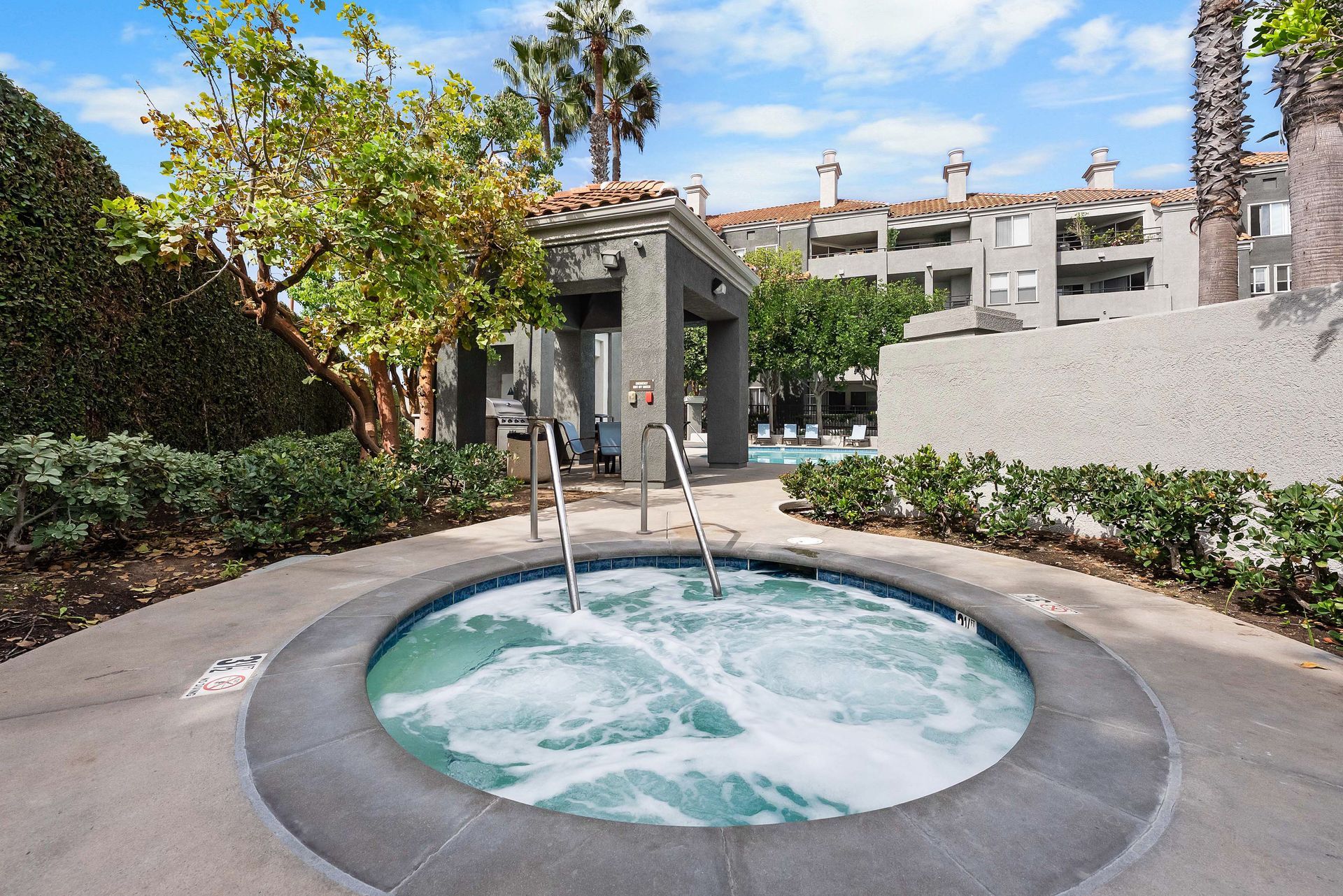 Hot tub with bubbling water, surrounded by landscaping, with apartments in the background.