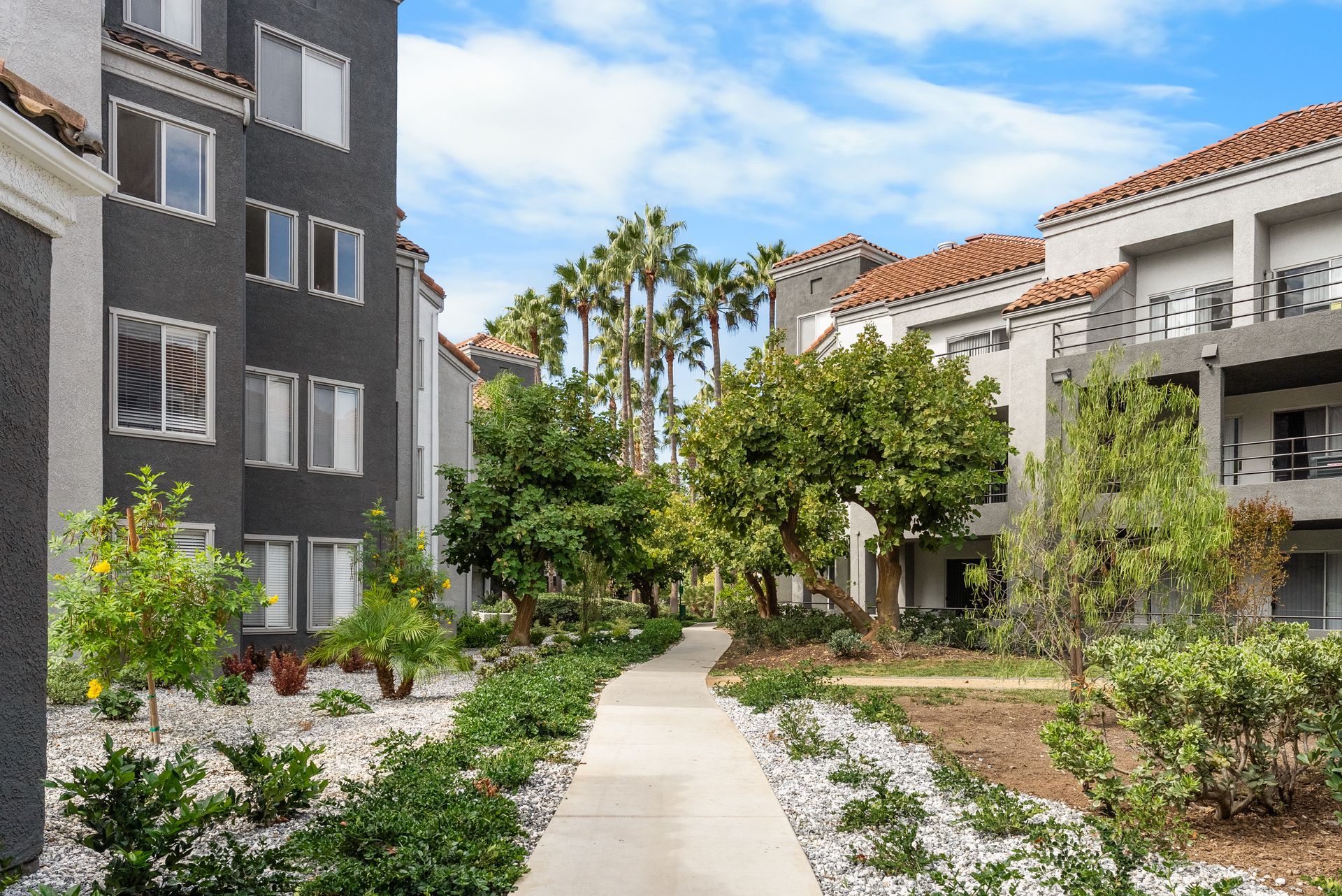 Courtyard with buildings, walkway, trees, and landscaping. Blue sky.