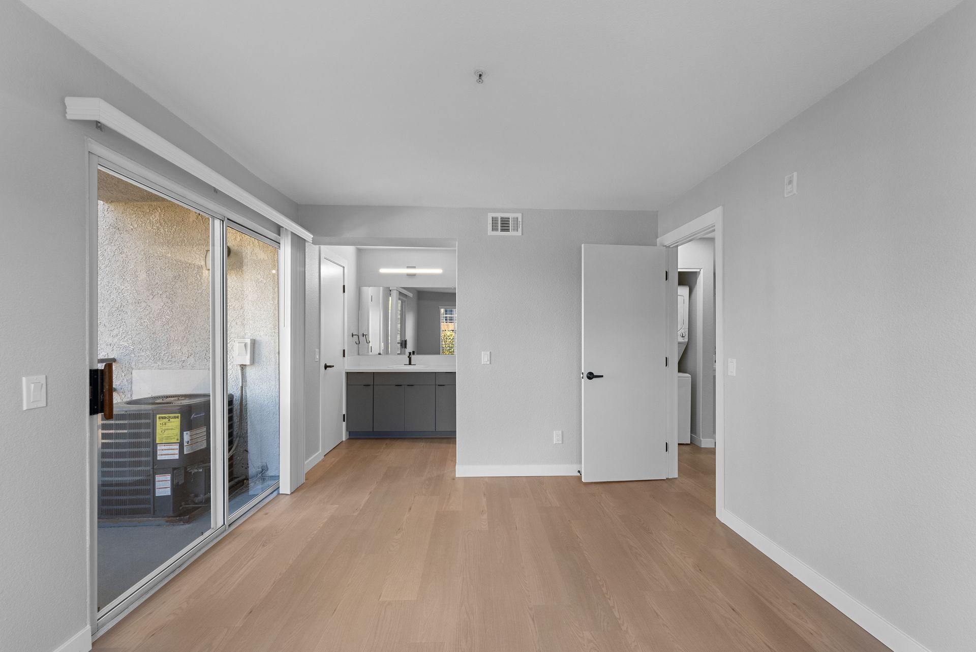 An empty bedroom room with hardwood floors and sliding glass doors leading to a balcony.