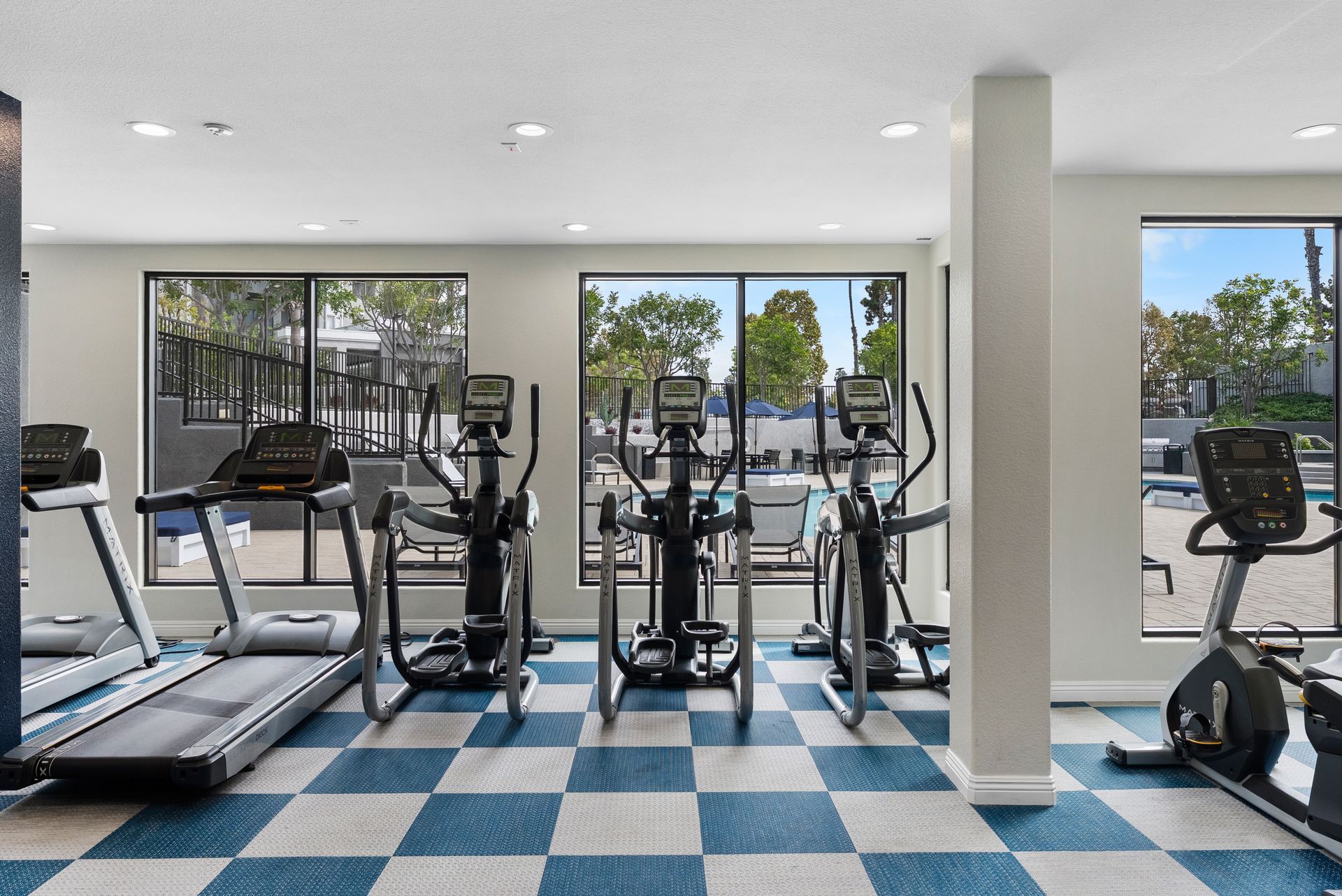 Gym with cardio machines, windows, and checkered blue and white floor.
