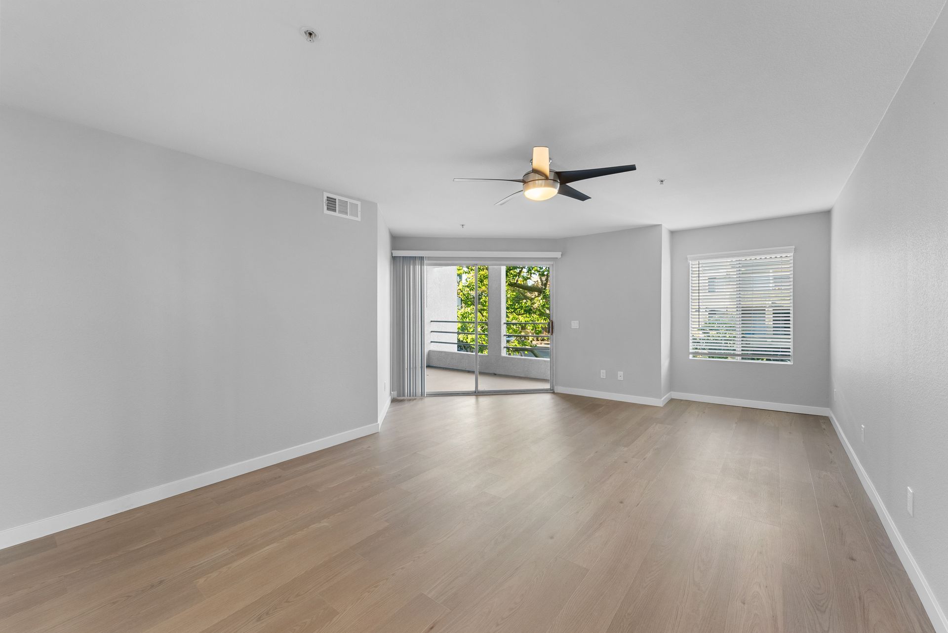 An empty living room with hardwood floors and a ceiling fan.