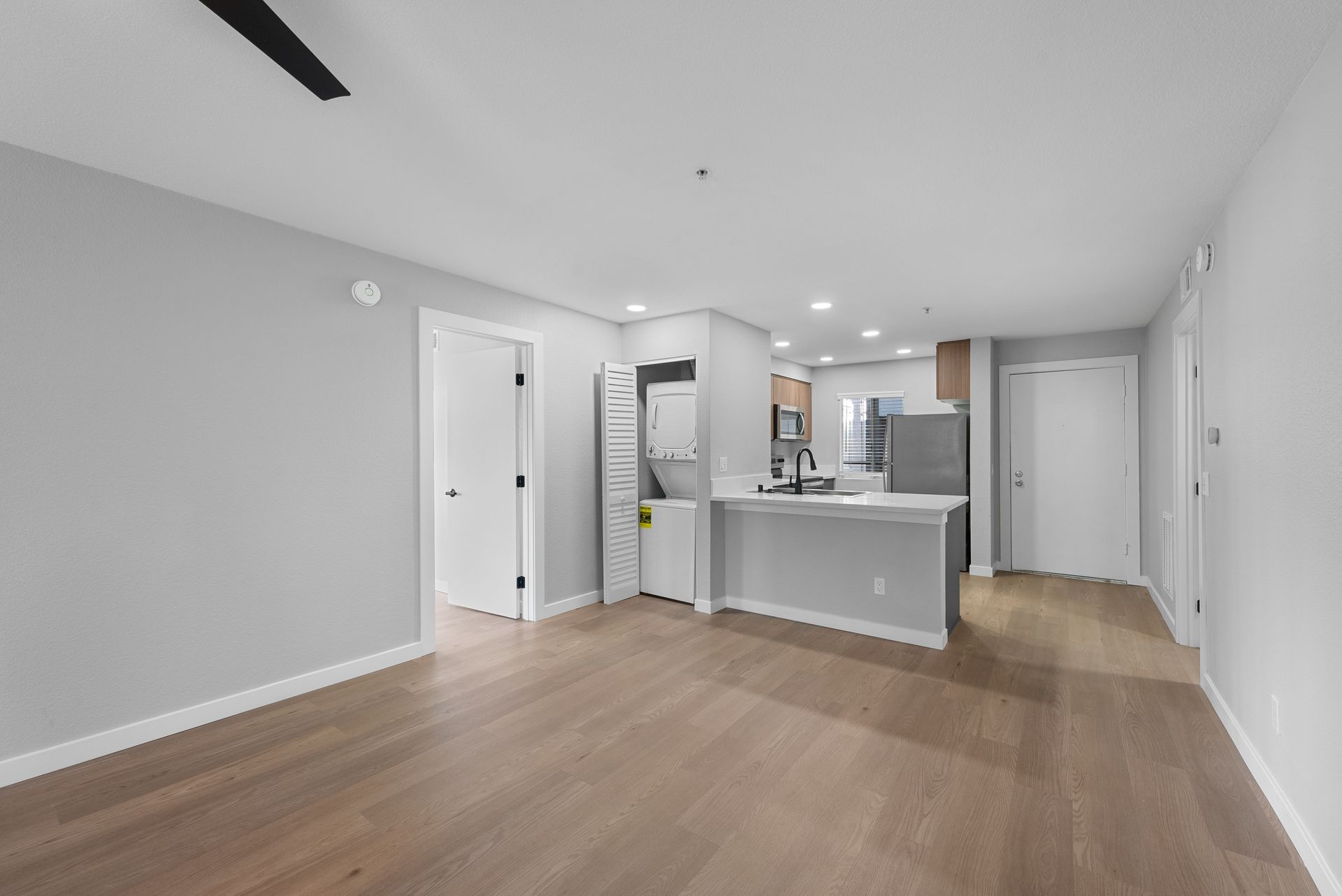 An empty living room with hardwood floors and a ceiling fan.