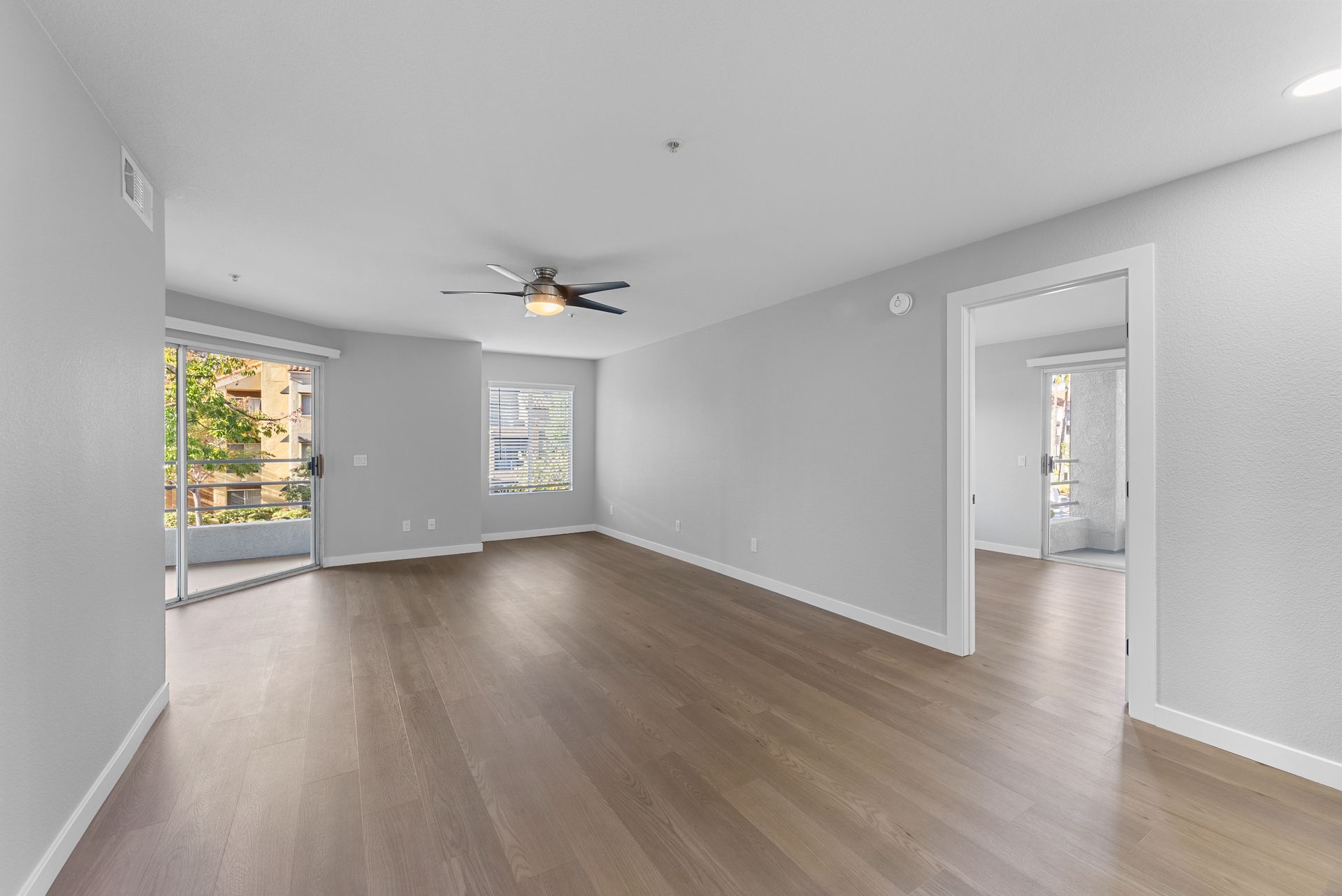 Open living room with wood floors, ceiling fan, and windows