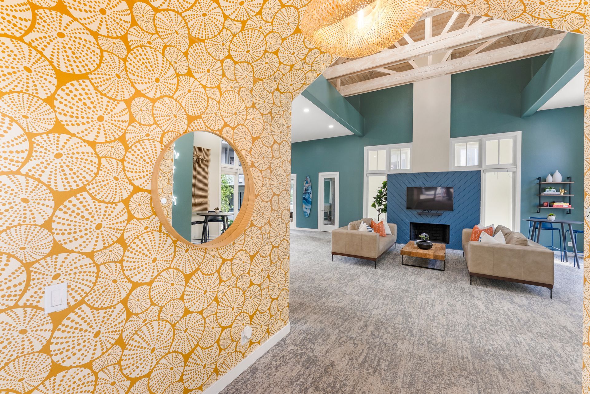Interior view: yellow patterned wallpaper, round mirror, teal wall with fireplace and seating area.