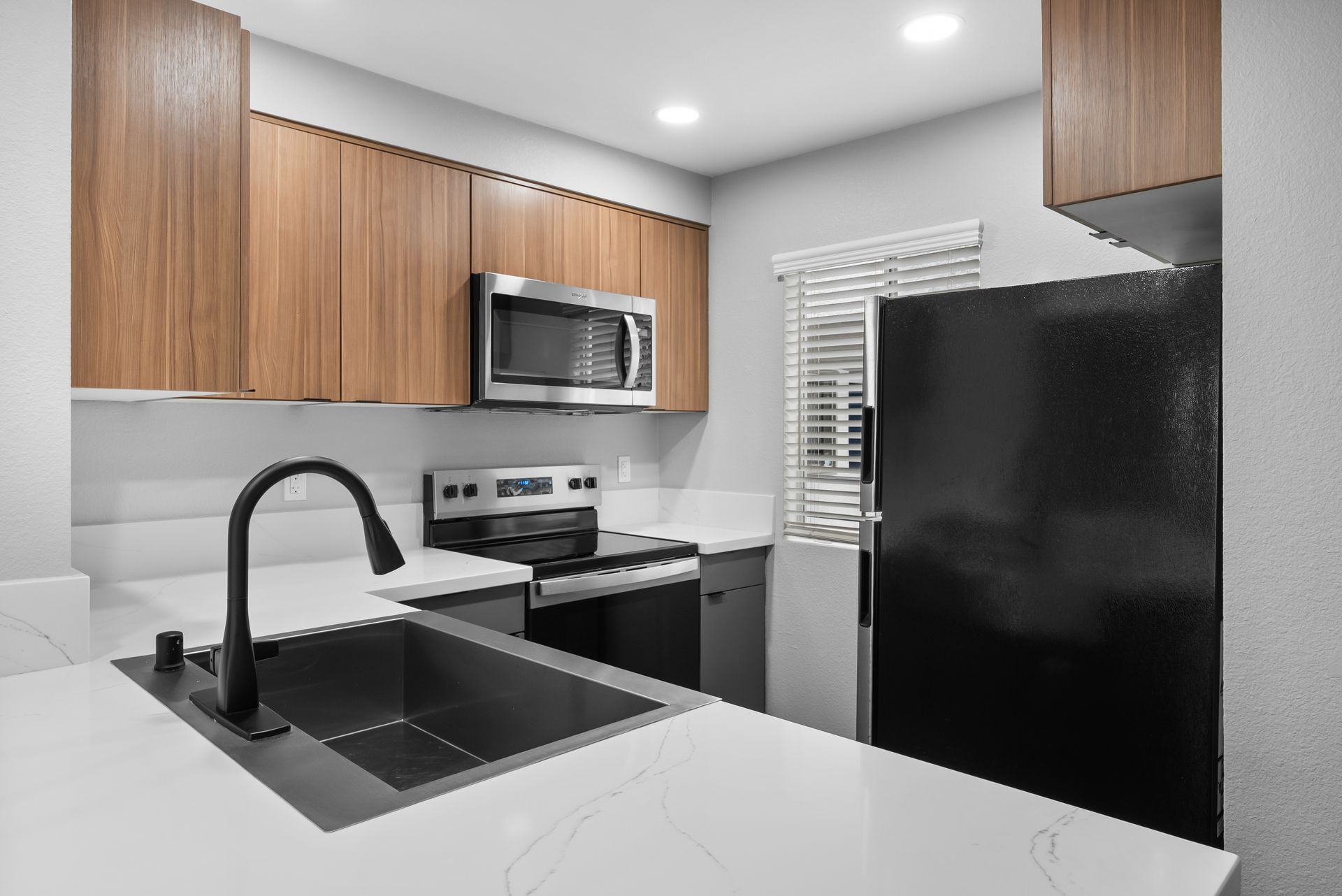 Modern kitchen with wood cabinets, black appliances, and white countertops.