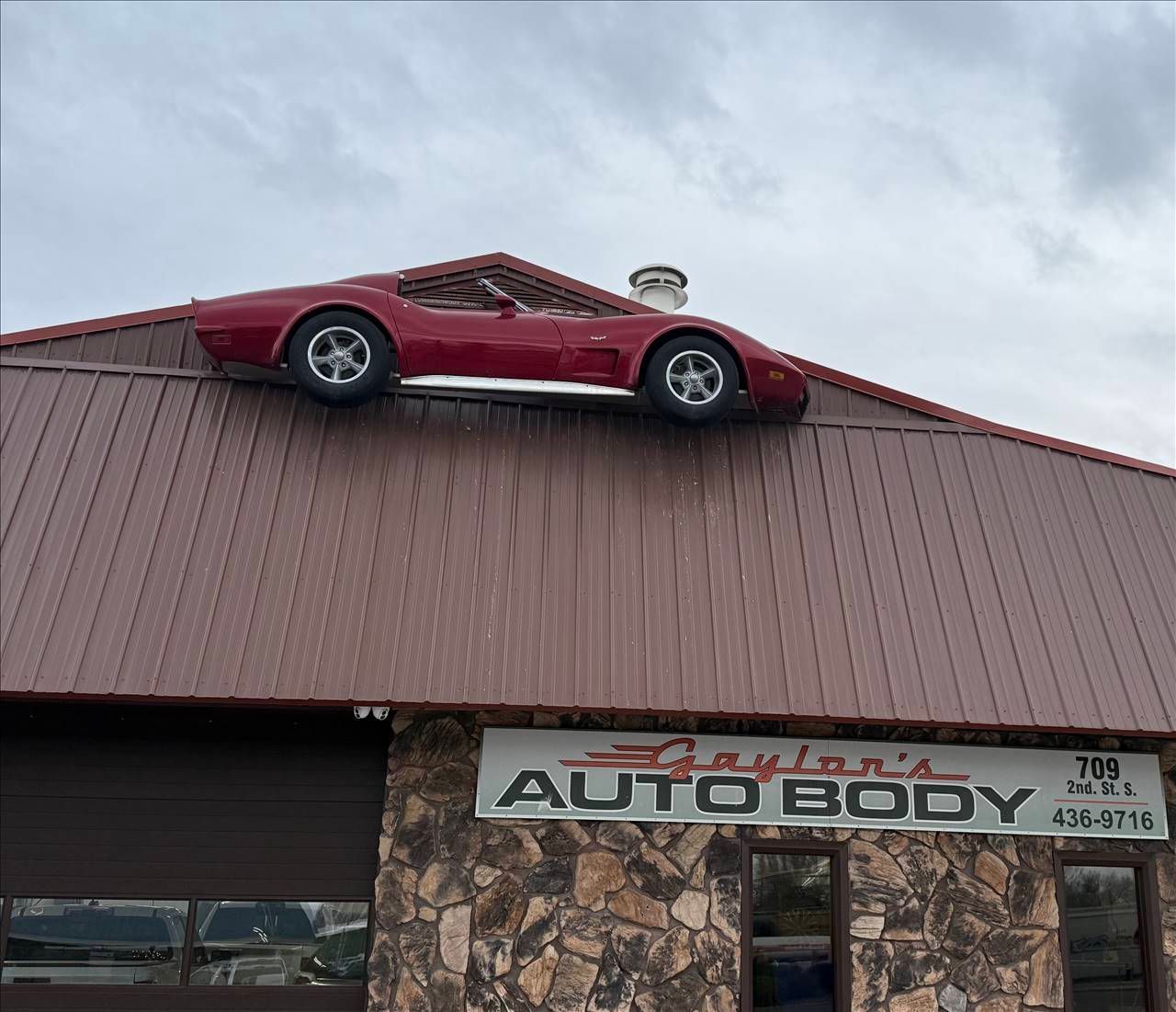 Red sports car displayed on the roof of an auto body shop building
